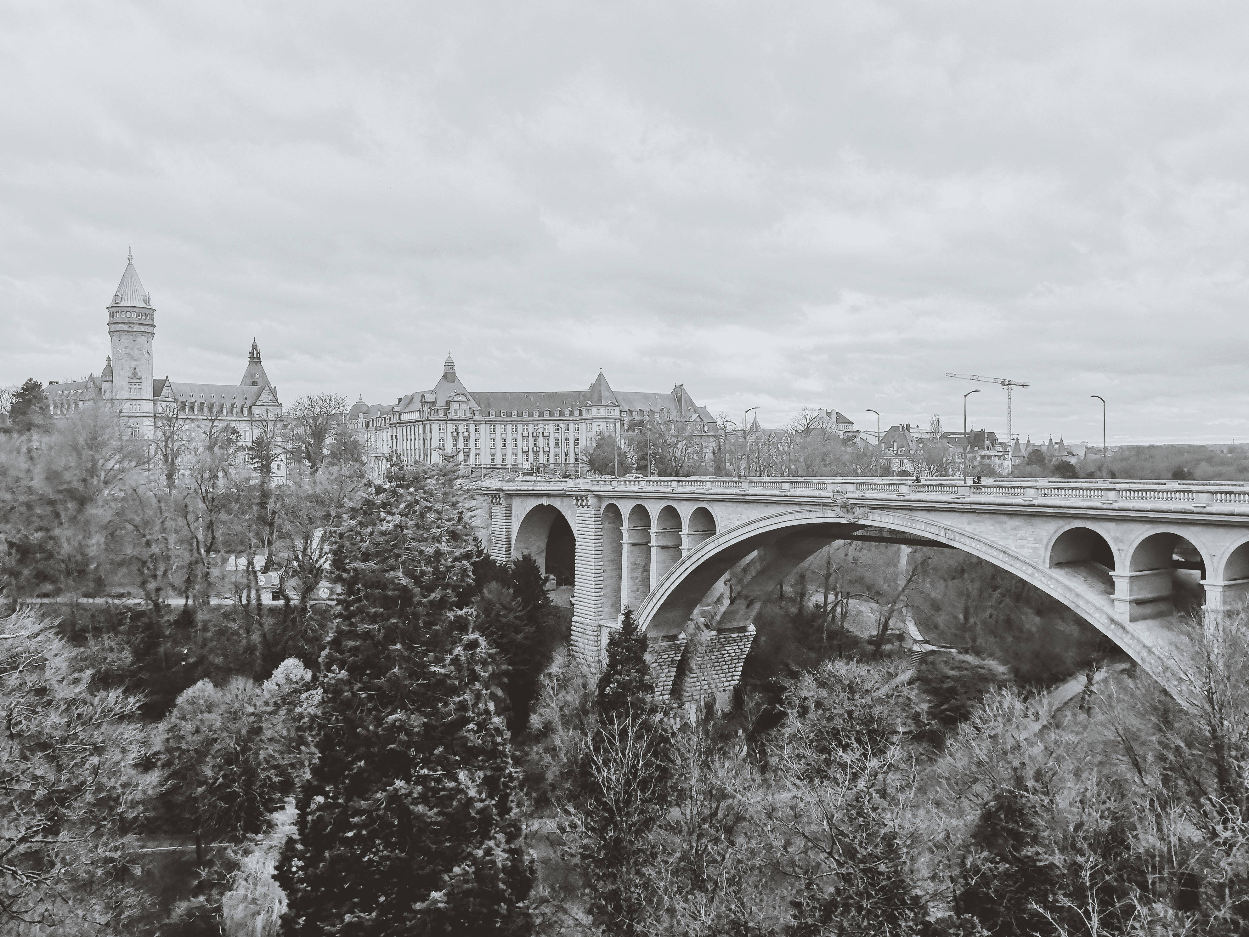 Luxembourg 桌布 壁紙 — 一座宏偉的石拱橋橫跨山谷，山谷中有歷史建築和無葉樹木，天空陰沉，呈現單色景觀。