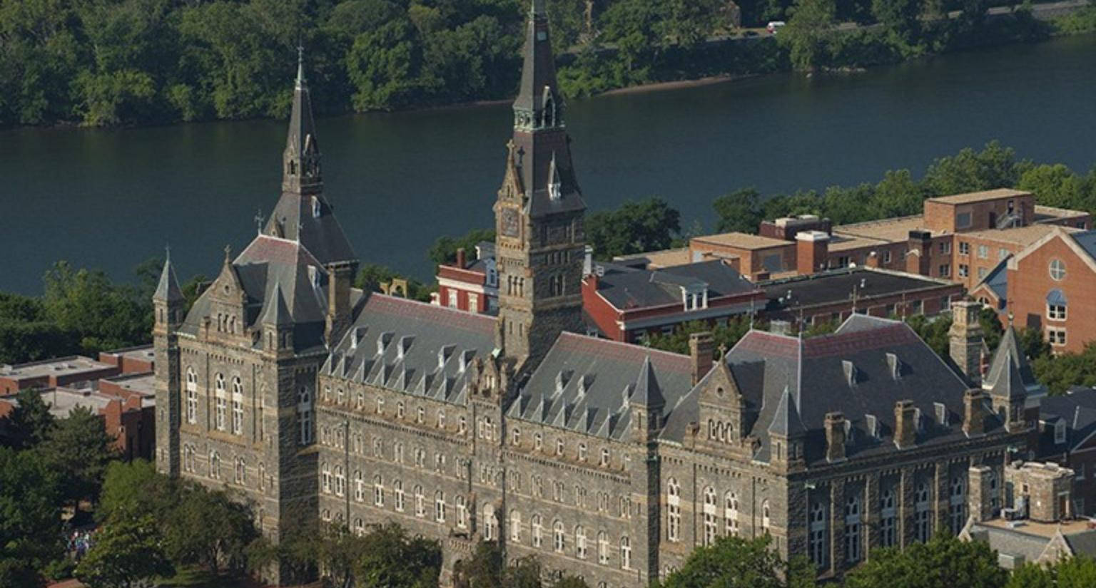 Architecture 桌布 壁紙 — 一座宏偉的石造大學建築，擁有雙塔，俯瞰著平靜的河流，周圍環繞著茂密的綠樹，鳥瞰圖。
