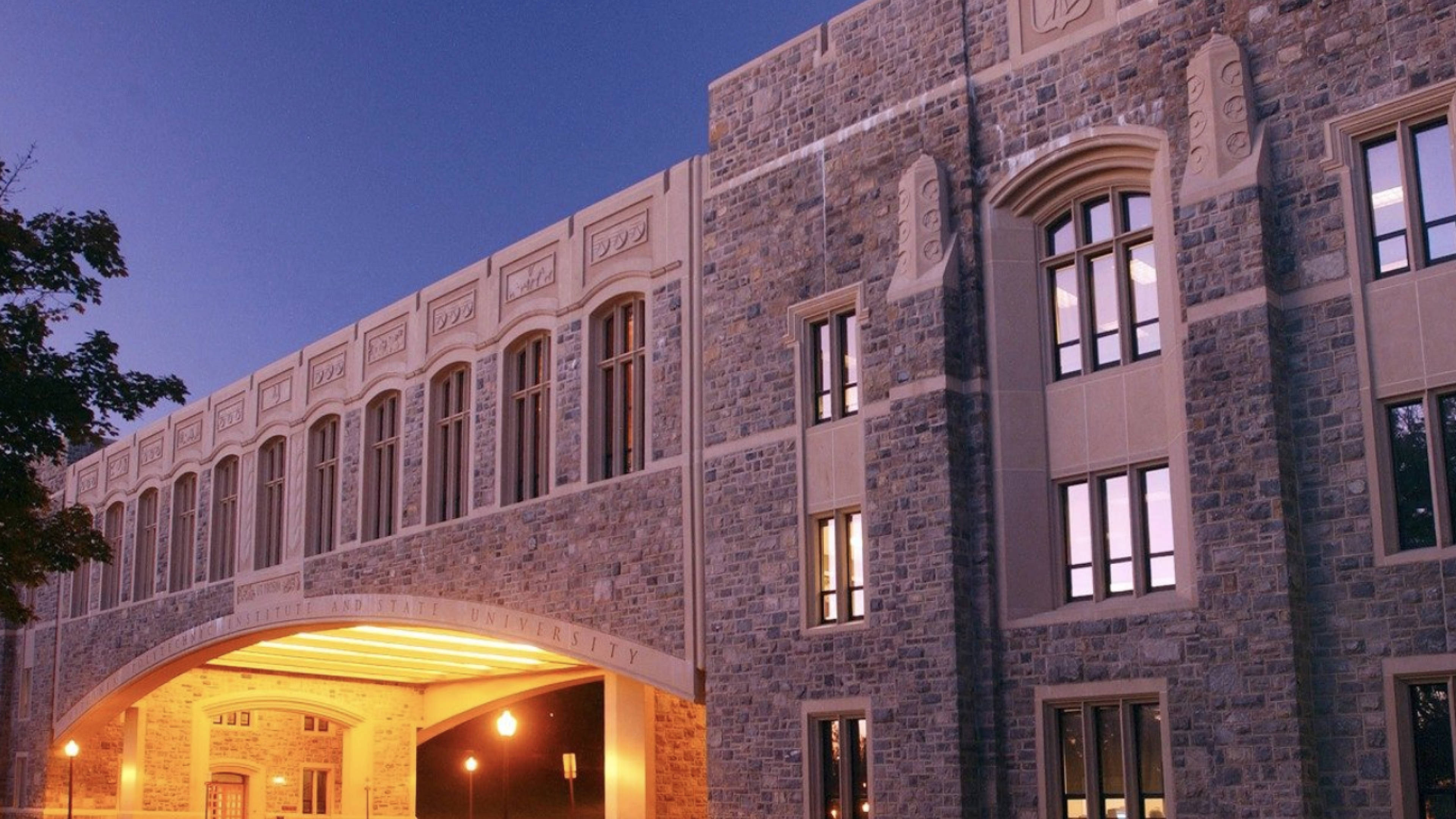 Virginia Tech 桌布 壁紙 — 一座宏偉的石造大學建築在黃昏時分亮起，窗戶和拱形入口透出溫暖燈光。