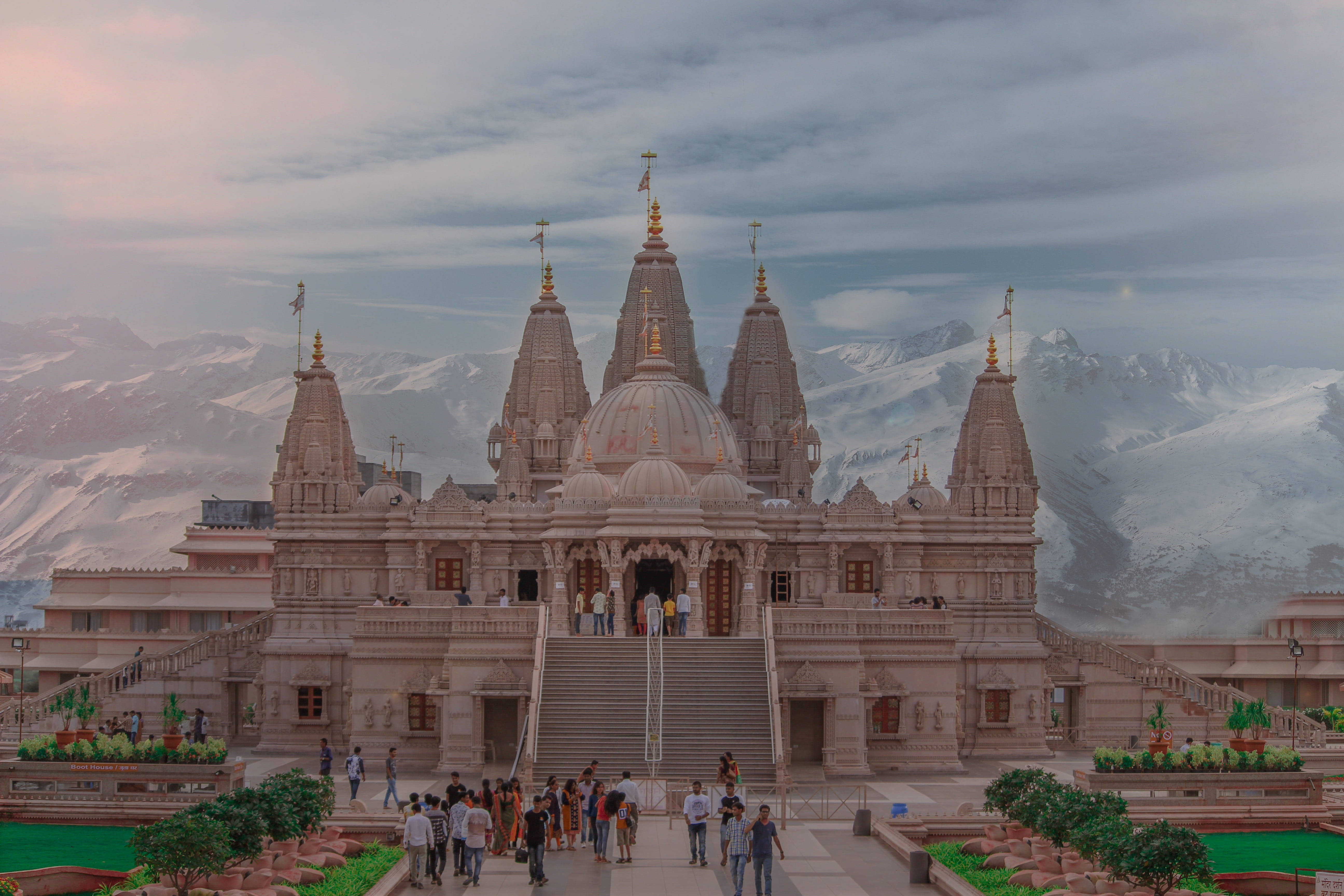 Mumbai 桌布 壁紙 — 一座宏偉的石造寺廟，金色尖塔在陰天背景下，雄偉地矗立在積雪覆蓋的山脈前。