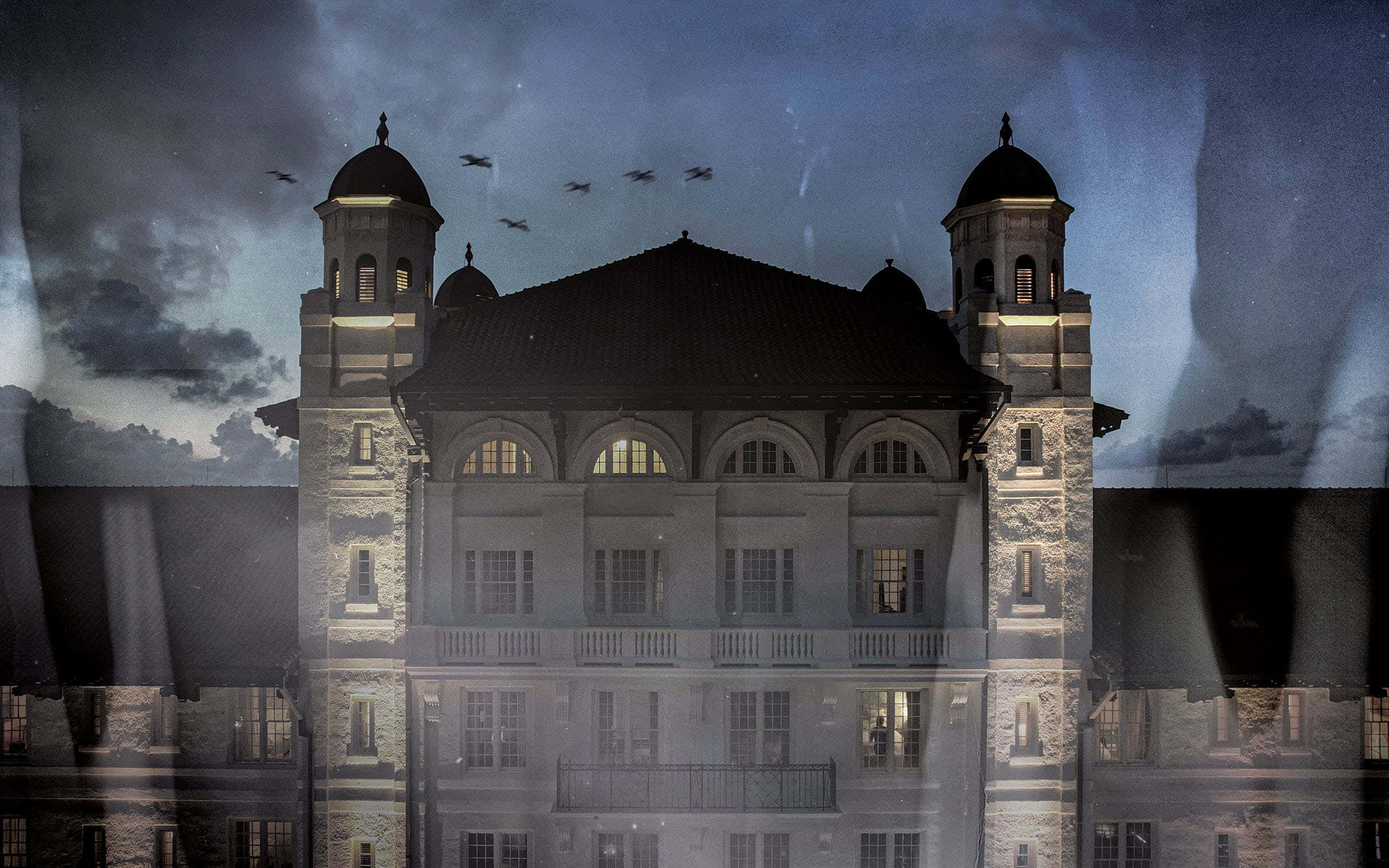 Haunted Hotels 桌布 壁紙 — 一座宏偉的石造建築，帶有圓頂塔樓，矗立在暴風雨暮色天空下，鳥兒在頭頂飛翔。