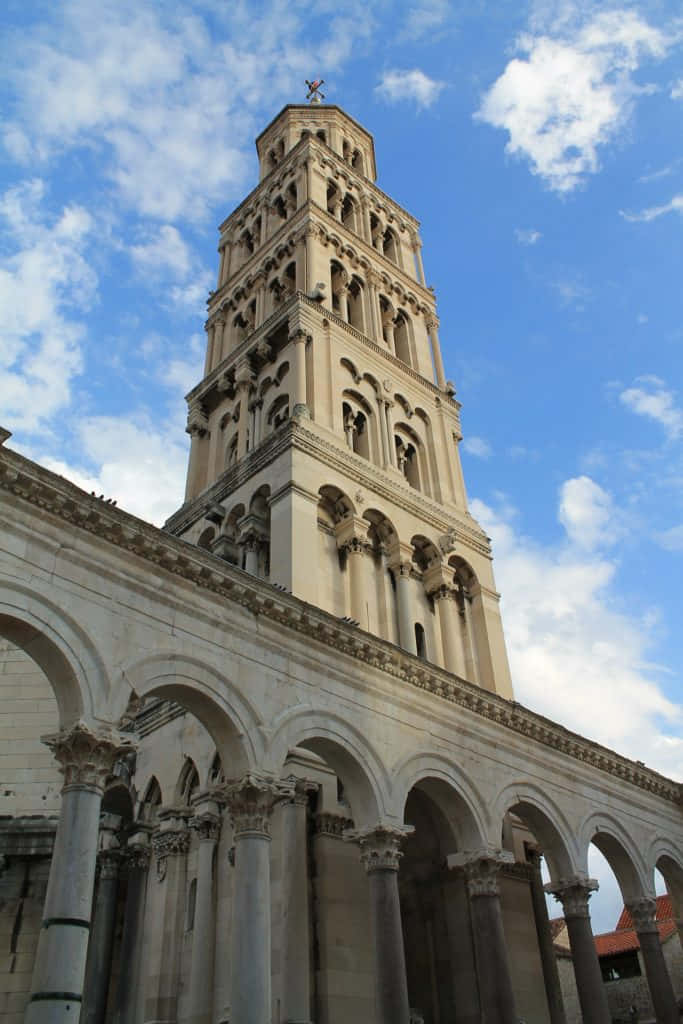 Croatia 桌布 壁紙 — 一座宏偉的石造鐘樓在藍天白雲下聳立，四周環繞著古典拱門和柱廊。