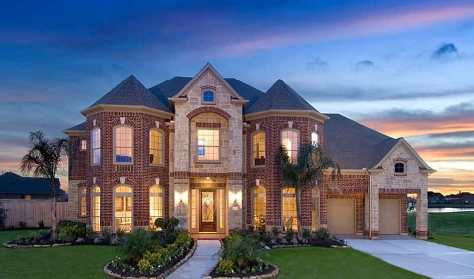 Mansion 桌布 壁紙 — 一座宏偉的磚砌豪宅，窗戶散發著溫暖的光芒，在暮色中雄偉地矗立在充滿活力的黃昏天空下。