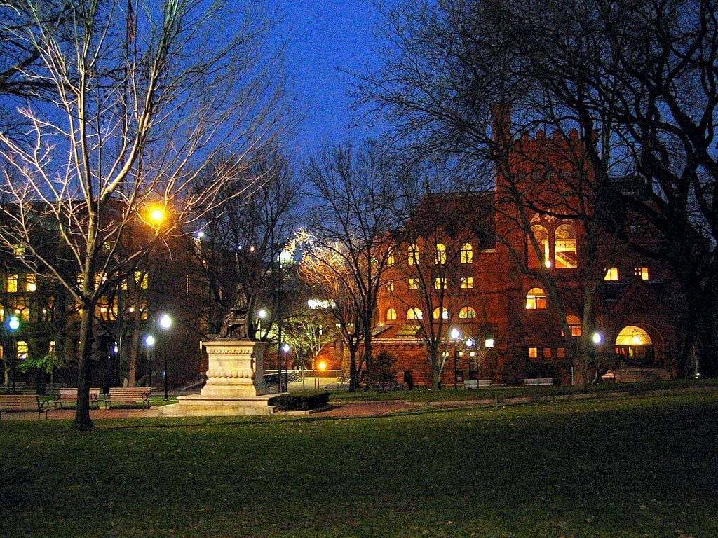 University Of Pennsylvania 桌布 壁紙 — 一座宏偉的磚造大學建築在黃昏時分溫暖地發光，光禿的樹木環繞著寧靜校園廣場中央的石碑。
