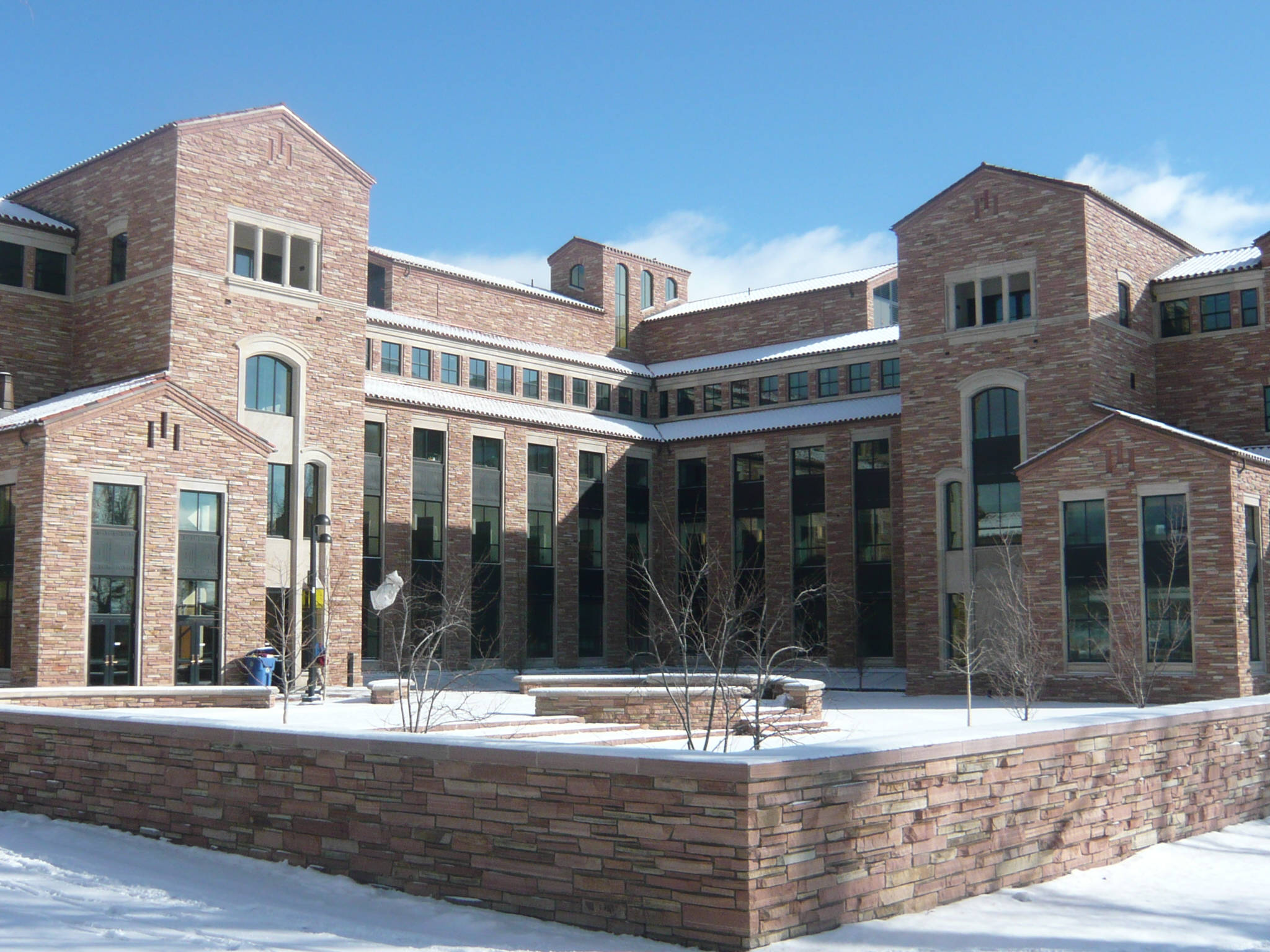 Colorado 桌布 壁紙 — 一座宏偉的磚造大學建築矗立在晴朗的藍天下，白雪覆蓋著地面和光禿的樹木。