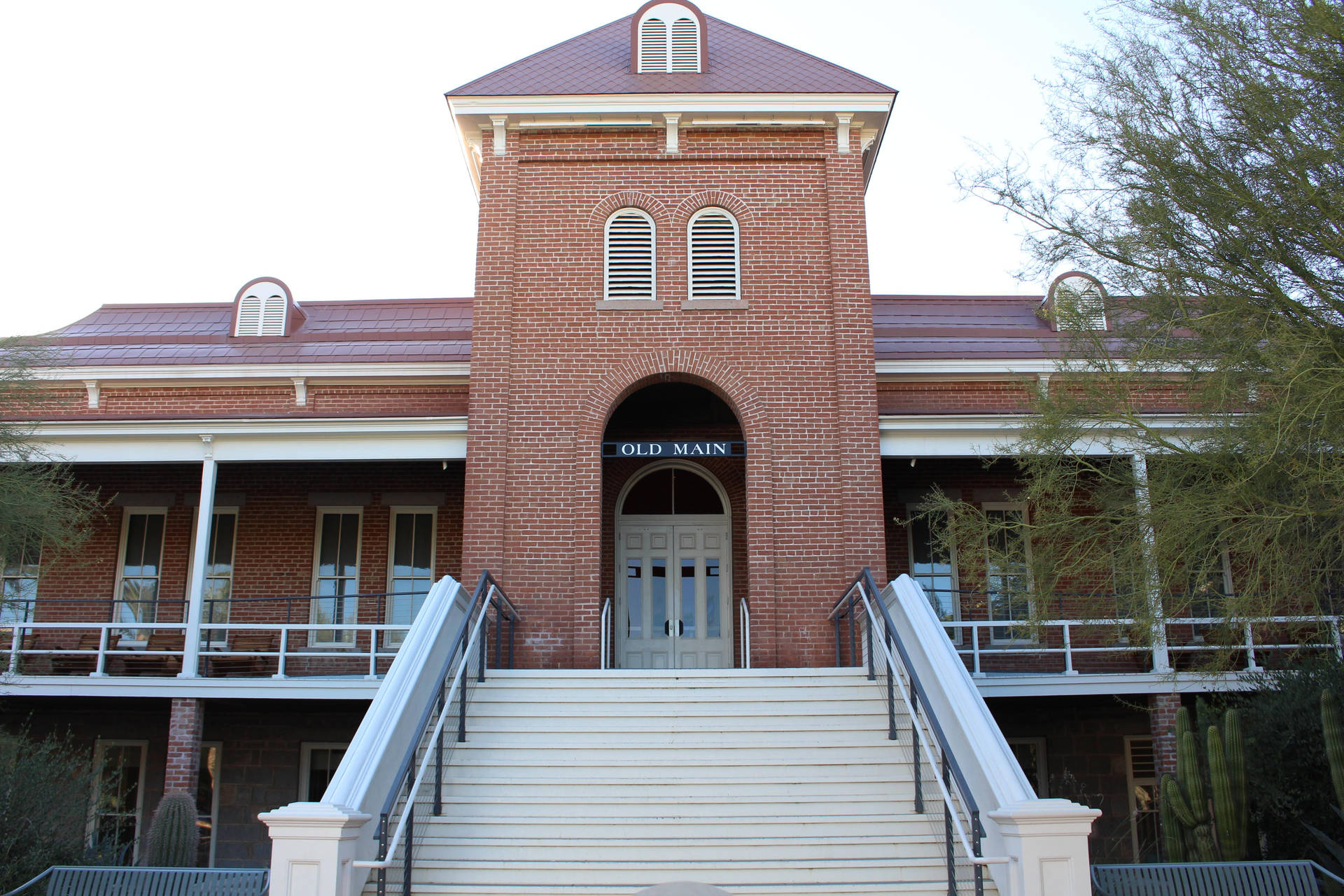  壁紙 — 一座宏偉的磚造建築，上面標有 'OLD MAIN'，有寬闊的白色樓梯和拱形窗戶，在明亮的天空下。
