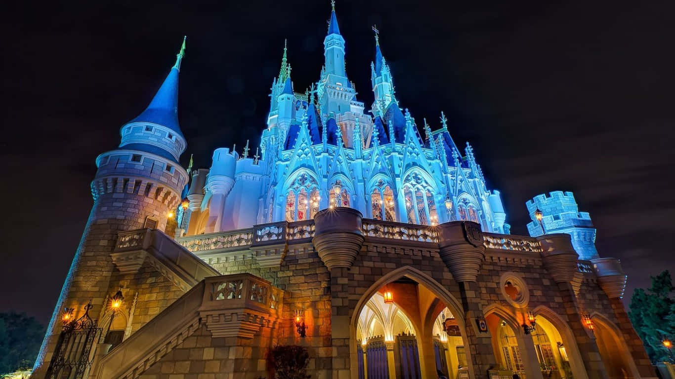 Cinderella Castle 桌布 壁紙 — 一座宏偉的童話城堡，在漆黑的夜空中閃耀著鮮豔的藍色和溫暖的金色燈光。