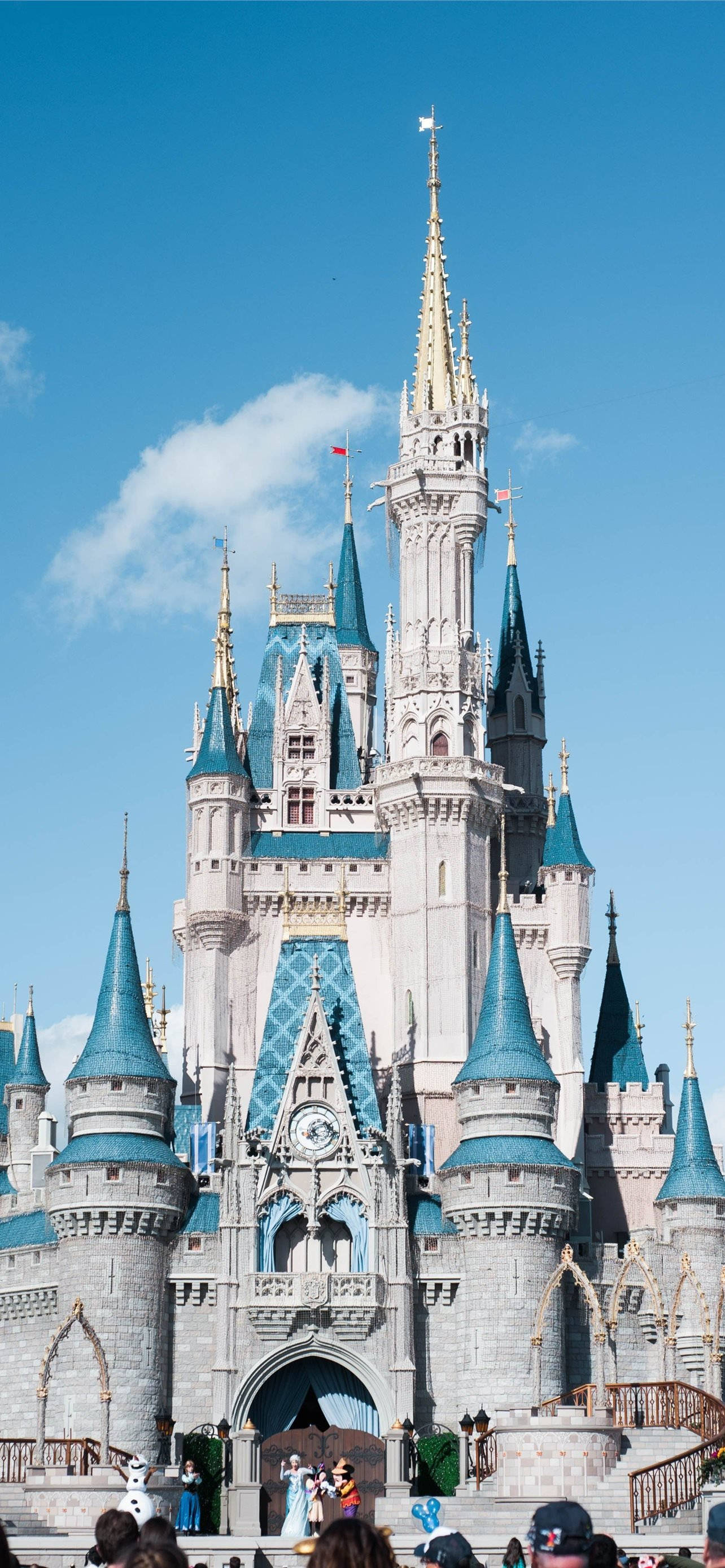 Disney Castle 桌布 壁紙 — 一座宏偉的童話城堡，擁有藍色圓錐形屋頂和金色尖塔，在晴朗的藍天和白雲下高高聳立。
