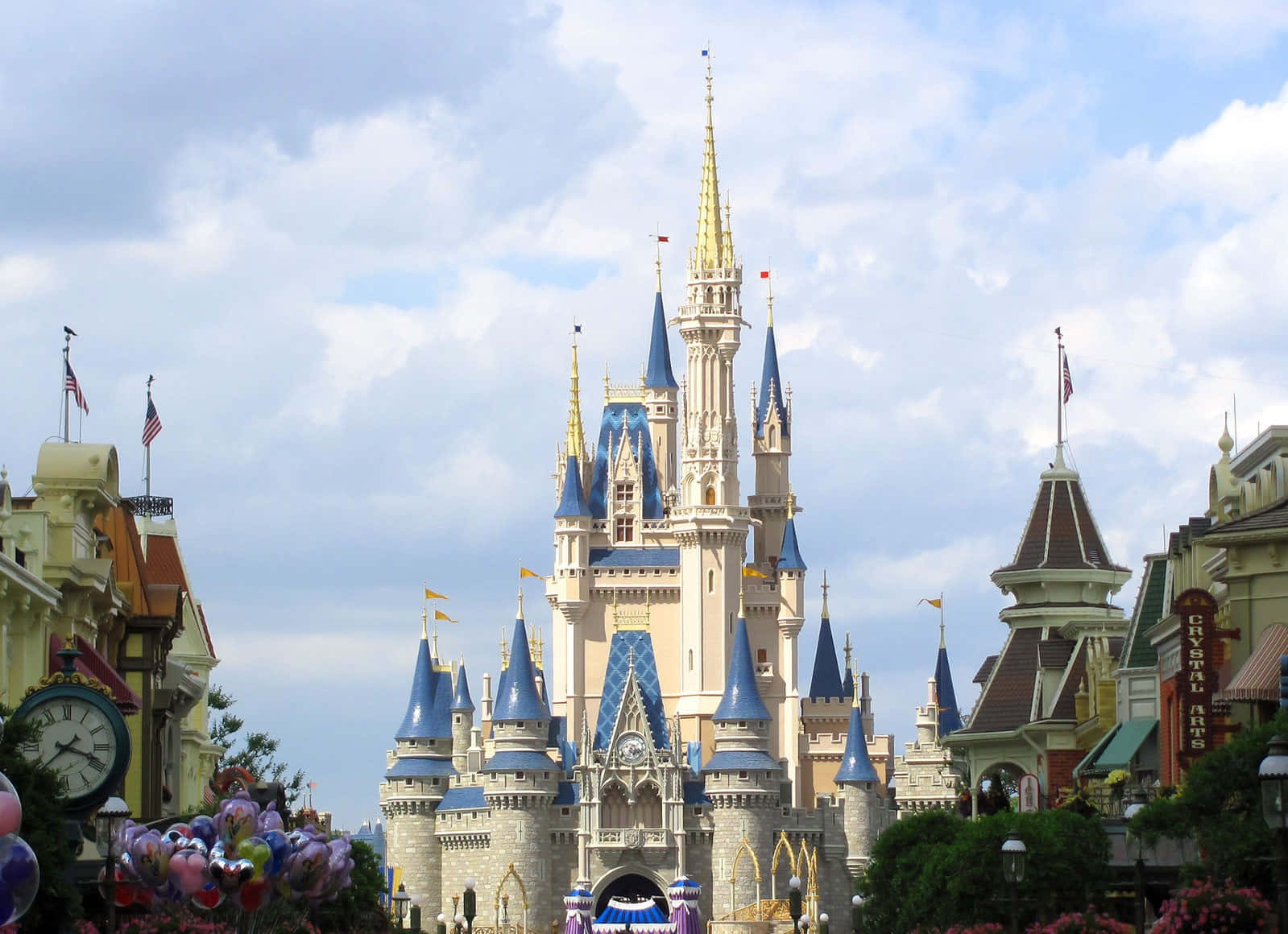 Disney Castle 桌布 壁紙 — 一座宏偉的童話城堡，擁有藍色尖頂和金色點綴，在部分多雲的天空下巍然聳立。