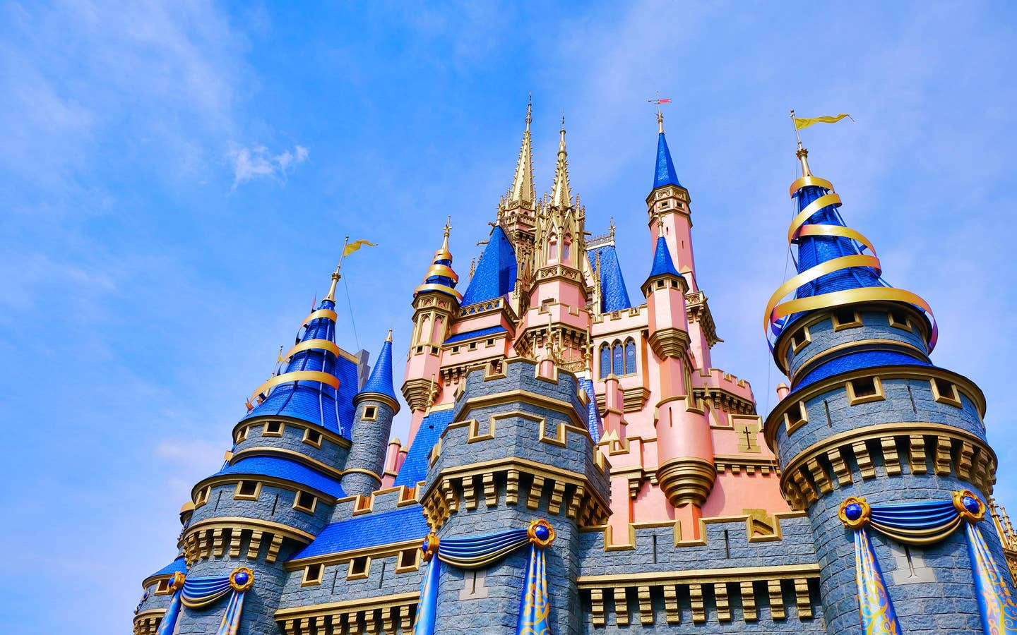Disney Castle 桌布 壁紙 — 一座宏偉的童話城堡，擁有藍色屋頂和粉紅色牆壁，在明亮的藍天下高聳入雲。
