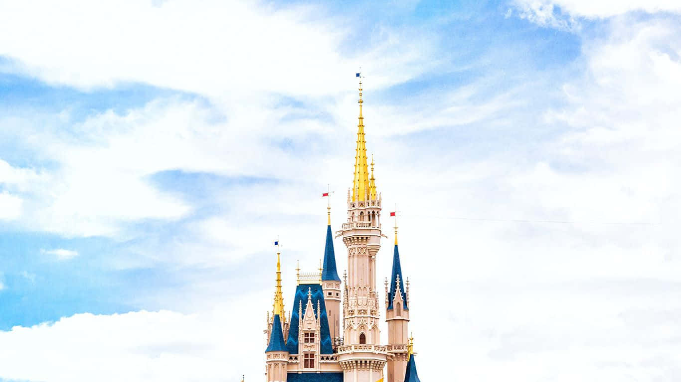 Cinderella Castle 桌布 壁紙 — 一座宏偉的童話城堡，擁有金色尖頂和藍色屋頂，在藍天白雲的映襯下巍然聳立。