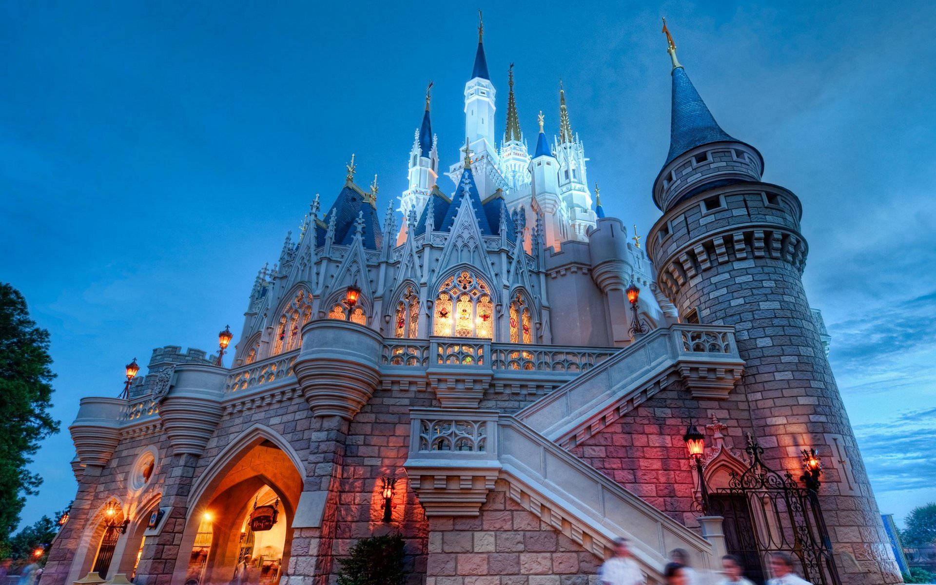 Disneyland Castle 桌布 壁紙 — 一座宏偉的童話城堡在黃昏時分被照亮，閃爍的窗戶和溫暖的燈籠映襯著深藍色的天空。