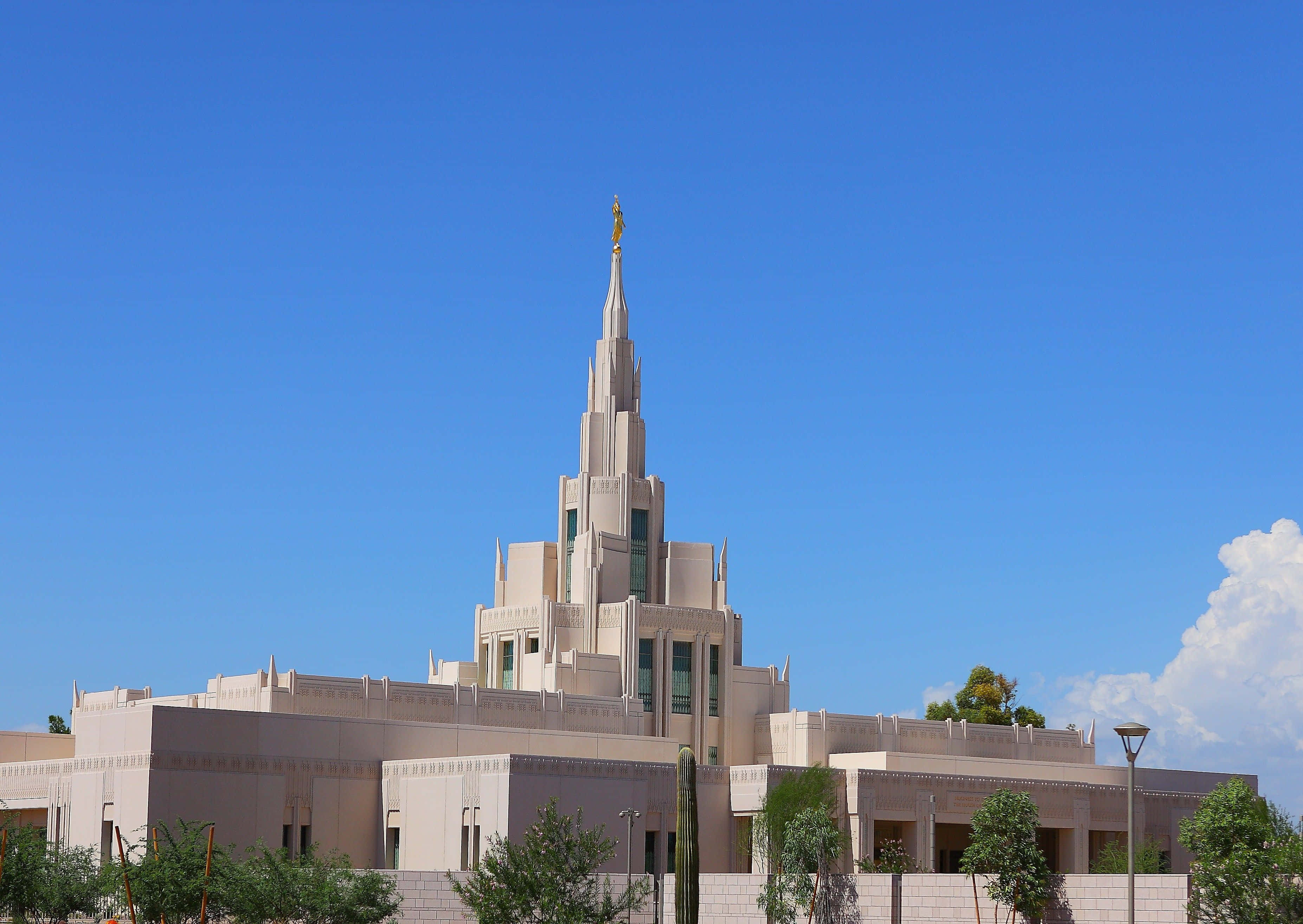 Phoenix Arizona 桌布 壁紙 — 一座宏偉的米色寺廟，擁有高聳的尖頂和金色雕像，矗立在晴朗的藍天和白雲之下。