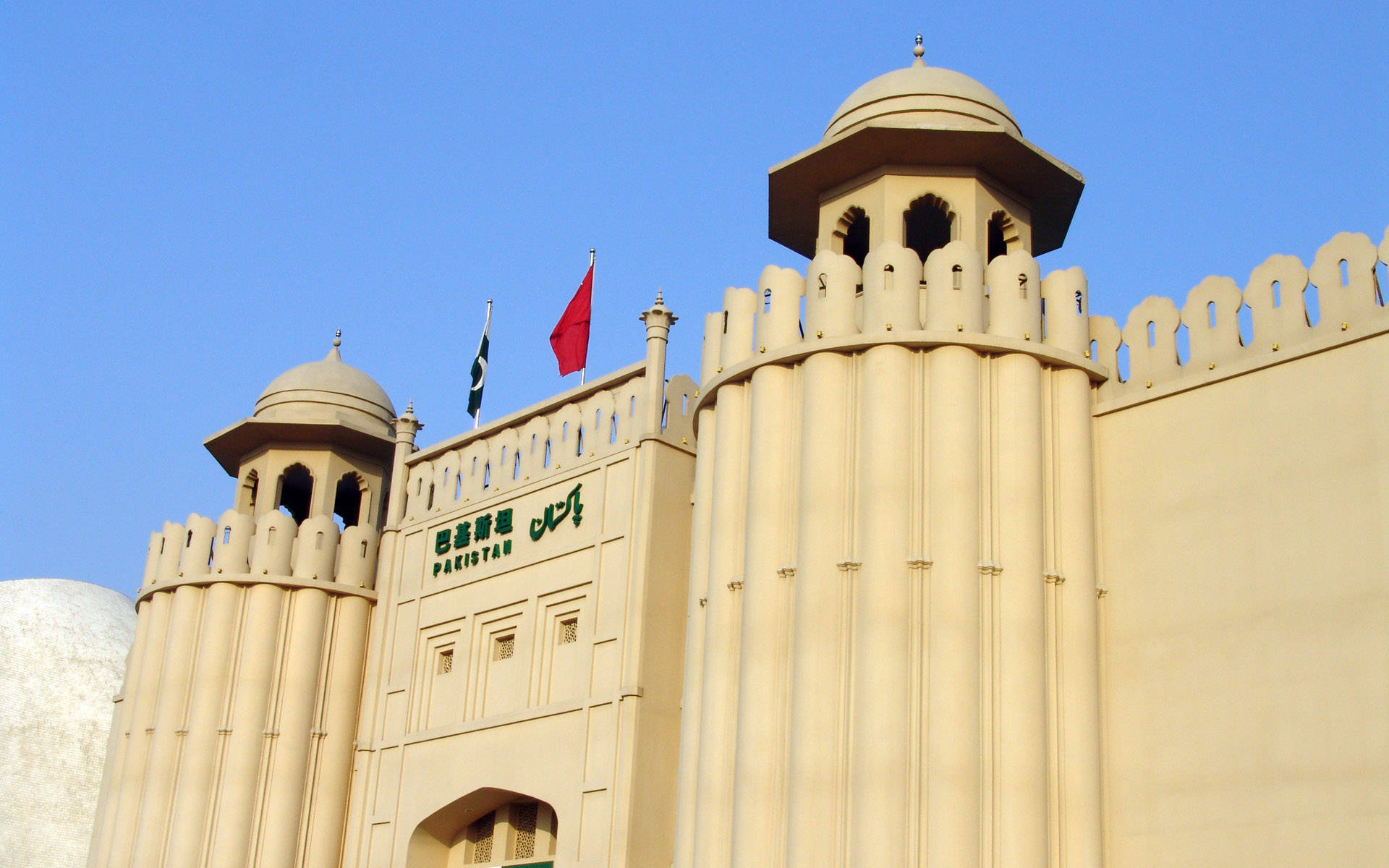 Pakistan 桌布 壁紙 — 一座宏偉的米色巴基斯坦政府建築，擁有圓頂塔樓和旗幟，背景是晴朗的藍天。
