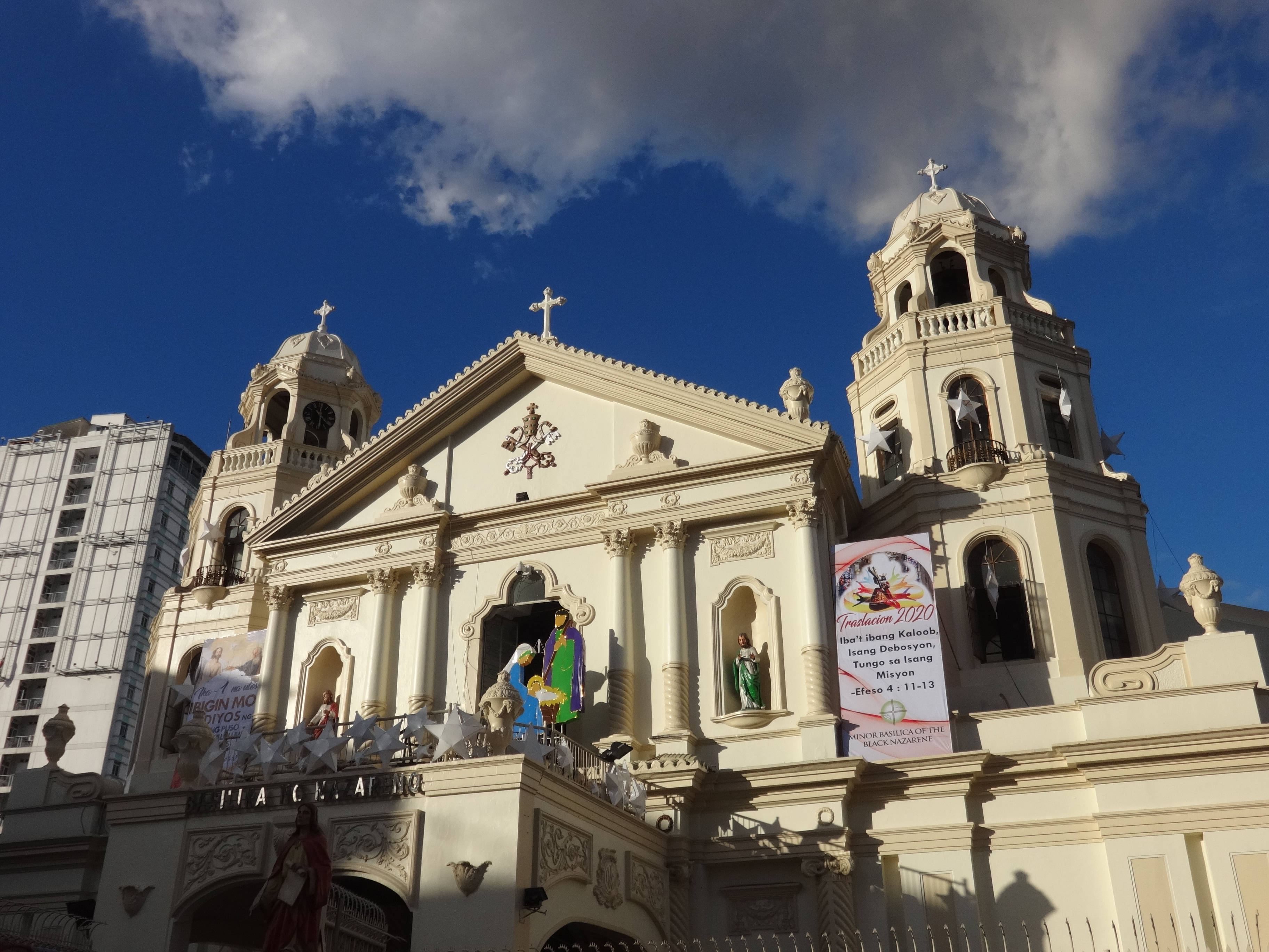 Manila 桌布 壁紙 — 一座宏偉的米色教堂，擁有雙鐘樓和華麗雕像，矗立在晴朗的藍天下，白雲朵朵。