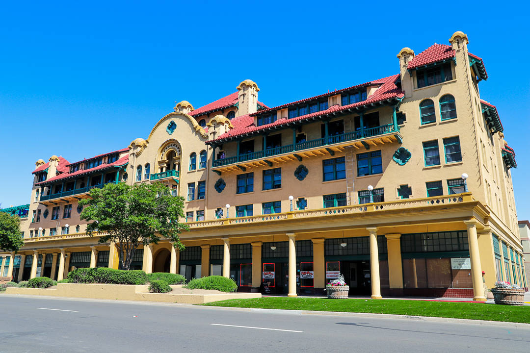 Hotel 桌布 壁紙 — 一座宏偉的米色西班牙復興風格建築，擁有紅色瓦片屋頂和拱形窗戶，矗立在晴朗的藍天下。