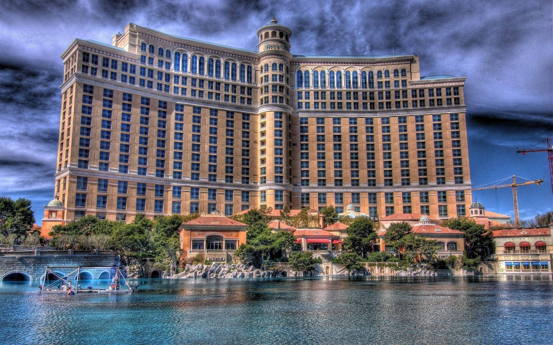 Las Vegas 桌布 壁紙 — 一座宏偉的米色飯店聳立在平靜的藍色潟湖之上，天空烏雲密佈，氣氛戲劇化。