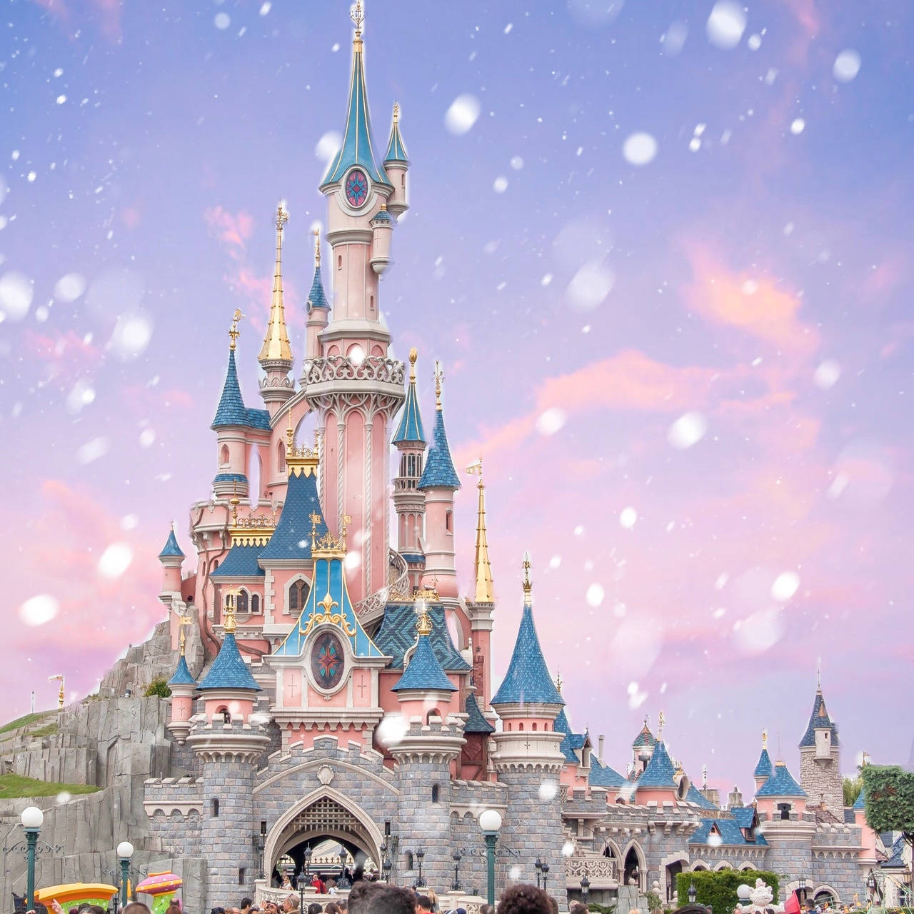 Disneyland Castle 桌布 壁紙 — 一座宏偉的粉紅色和藍色城堡，帶有金色尖塔，矗立在夢幻般的暮色天空下，柔軟的雪花輕輕飄落。