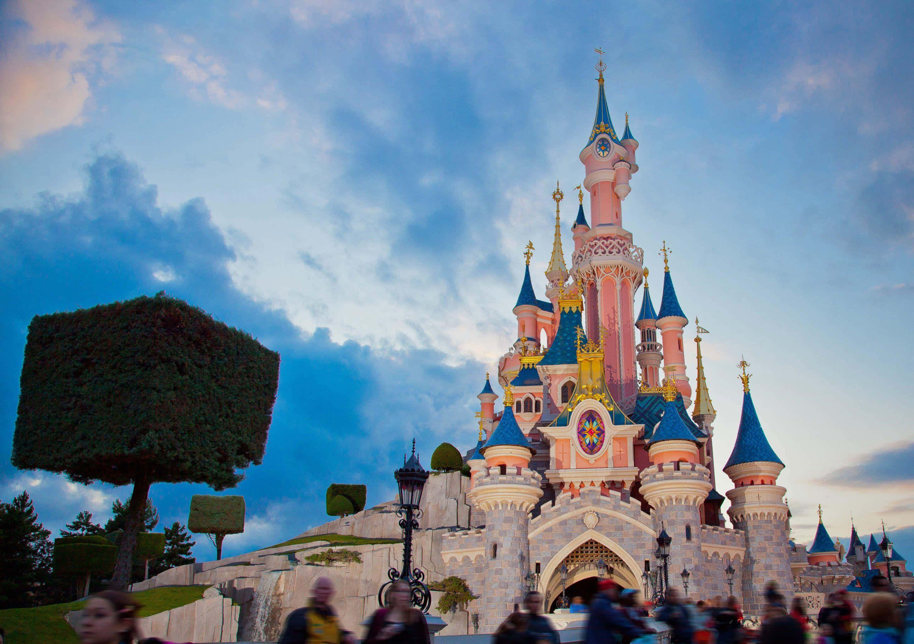 Disneyland 桌布 壁紙 — 一座宏偉的粉紅色和藍色城堡，金色尖塔在暮色天空和散落的雲朵中巍然聳立。