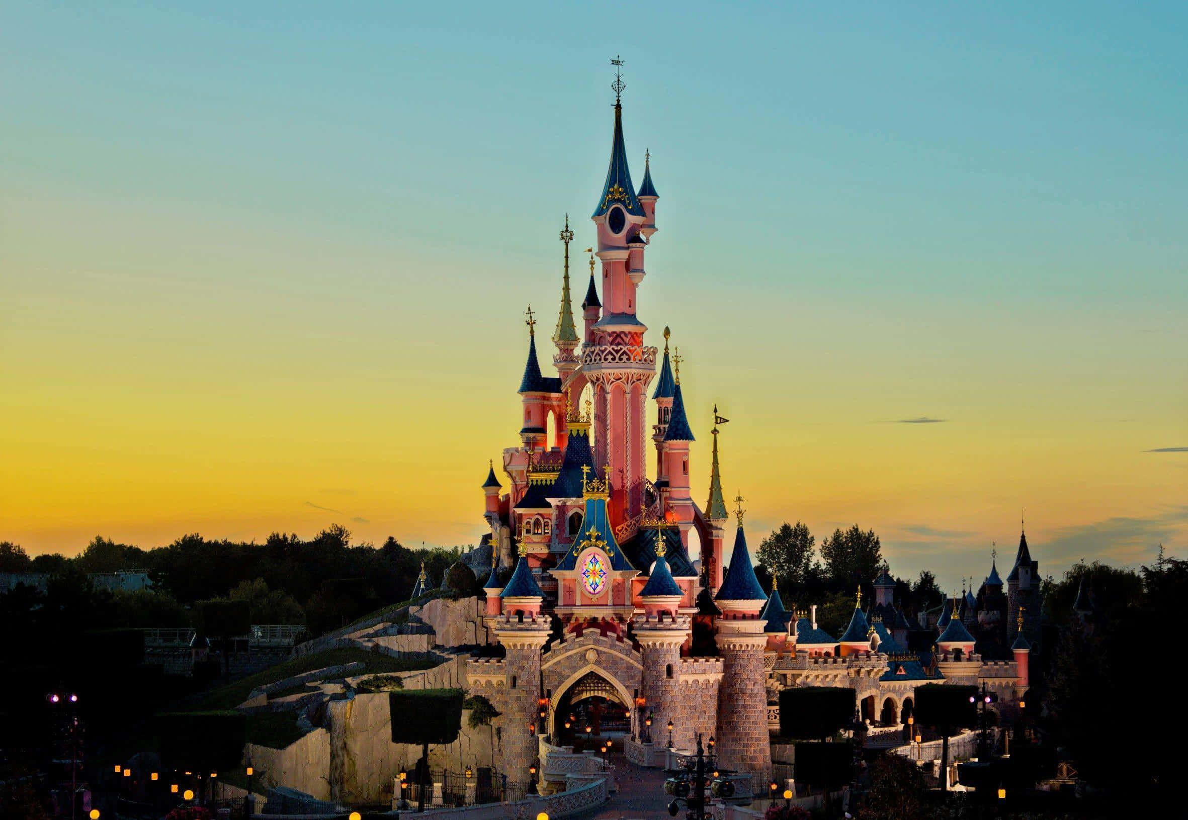 Disneyland 桌布 壁紙 — 一座宏偉的粉紅色城堡，帶有藍色尖頂，在金色夕陽天空下閃耀。