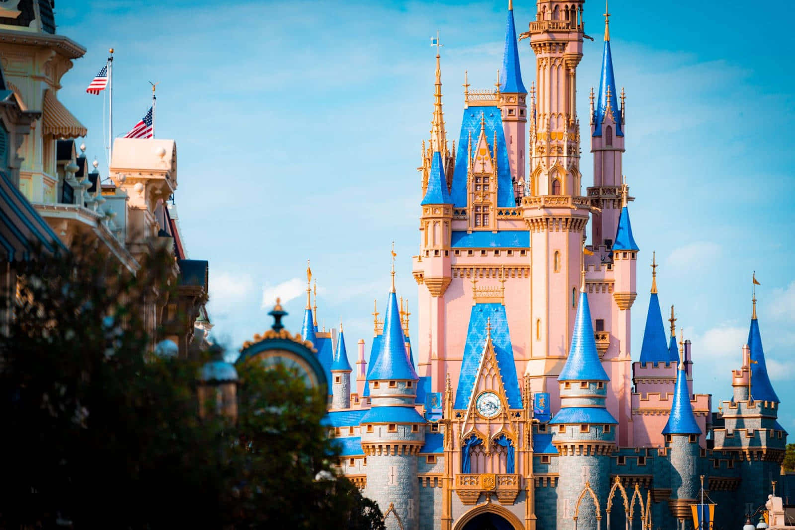 Disney Castle 桌布 壁紙 — 一座宏偉的粉紅色城堡，帶有藍色尖頂和金色裝飾，在晴朗的藍天下高高聳立。