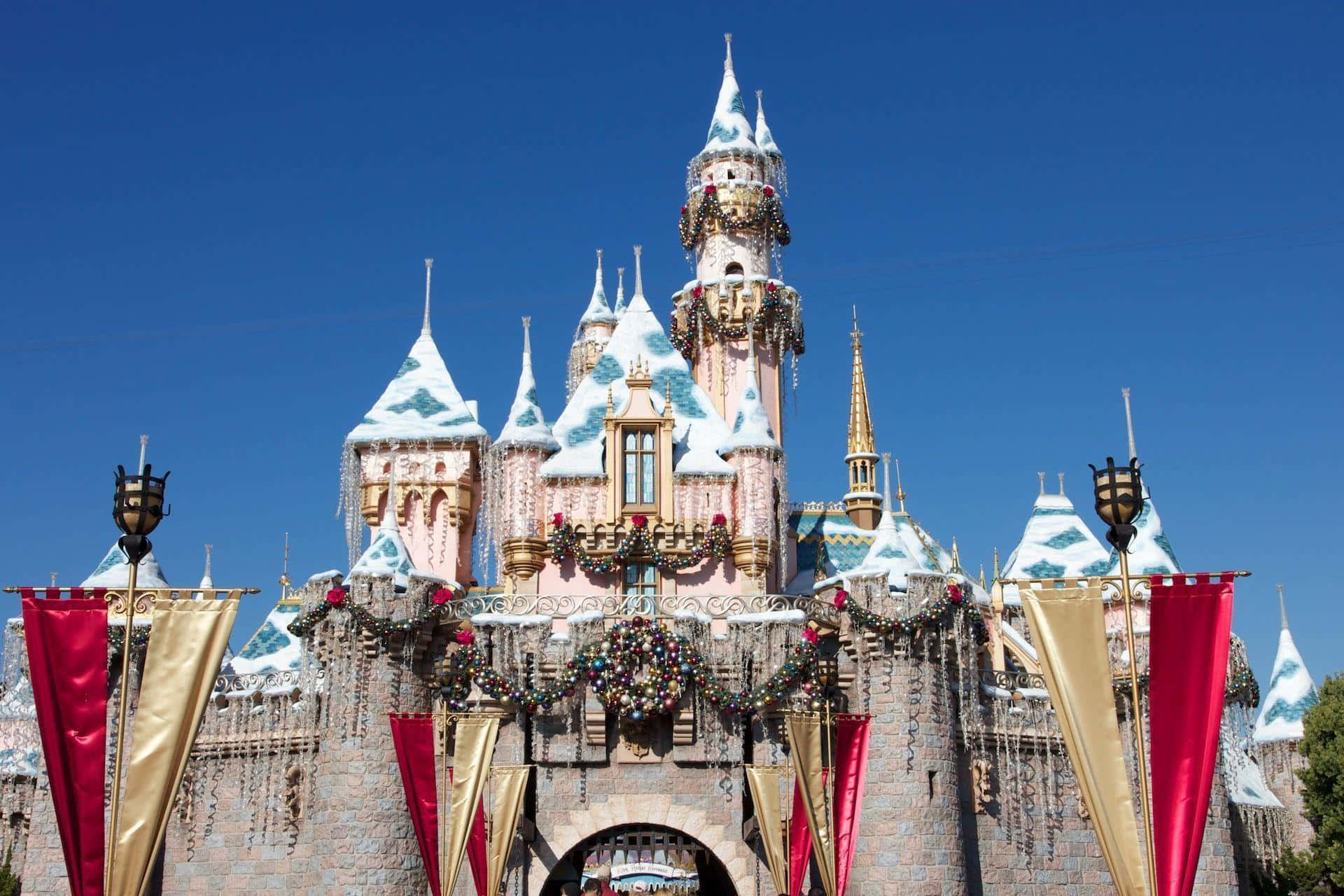 Disneyland 桌布 壁紙 — 一座宏偉的粉紅色城堡，擁有積雪的塔樓和節日花環，矗立在清澈的藍天下。
