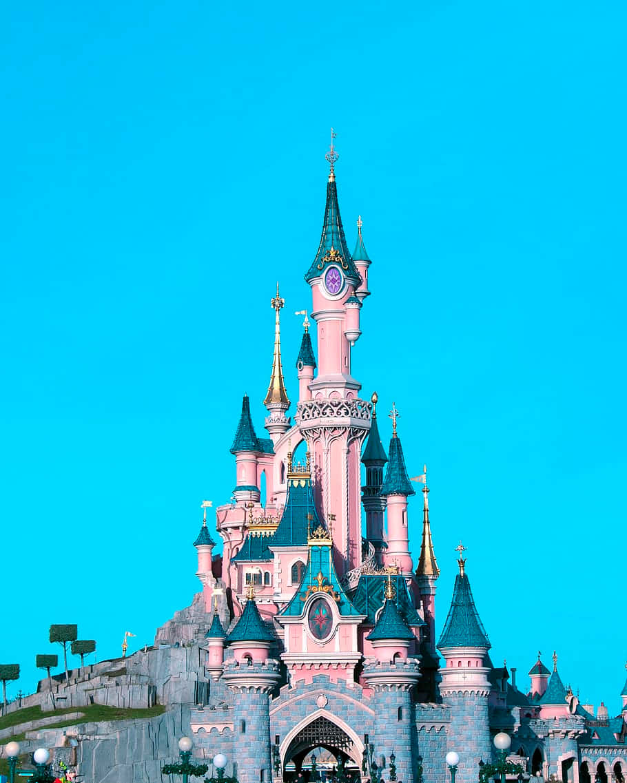 Disneyland Castle 桌布 壁紙 — 一座宏偉的粉紅色城堡，擁有藍綠色屋頂和金色尖塔，聳立在充滿活力的青色天空下。