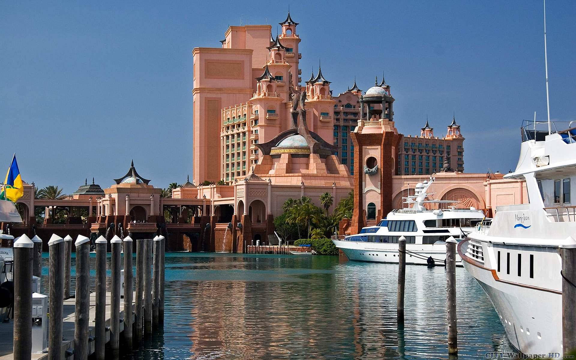 Nassau Bahamas 桌布 壁紙 — 一座宏偉的粉紅色度假城堡聳立在碼頭之上，豪華遊艇在清澈的藍天下停泊。