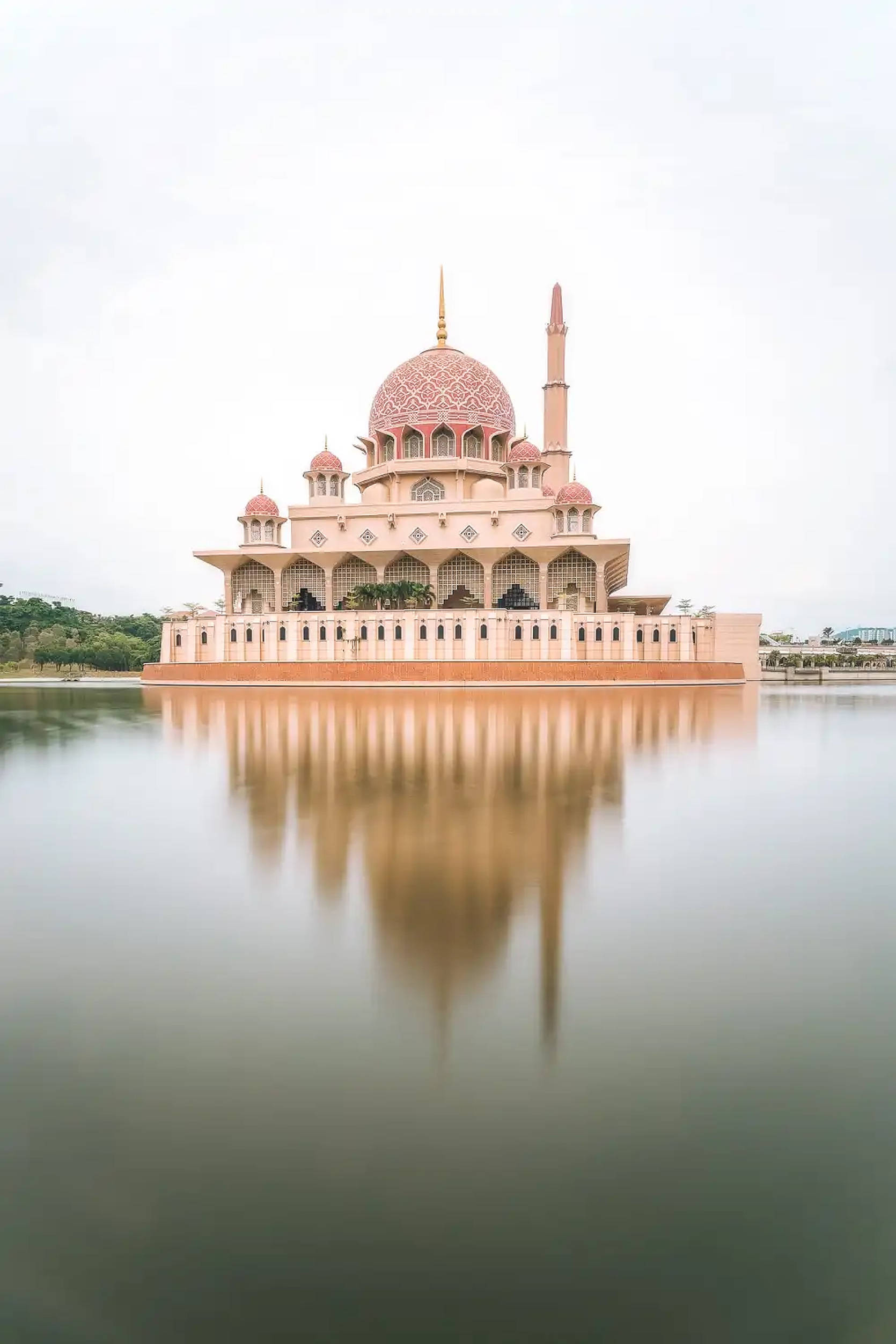 Kuala 桌布 壁紙 — 一座宏偉的粉紅色清真寺，擁有精緻的圓頂和宣禮塔，完美倒映在陰天下的平靜水面上。