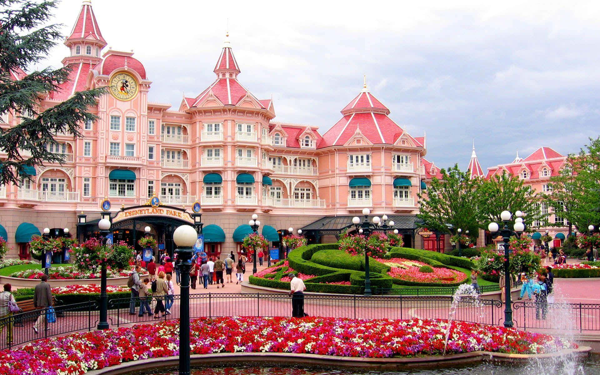 Disneyland 桌布 壁紙 — 一座宏偉的粉紅色迪士尼酒店，擁有紅色屋頂和修剪整齊的花園，在陰天之下開滿了鮮豔的花朵。