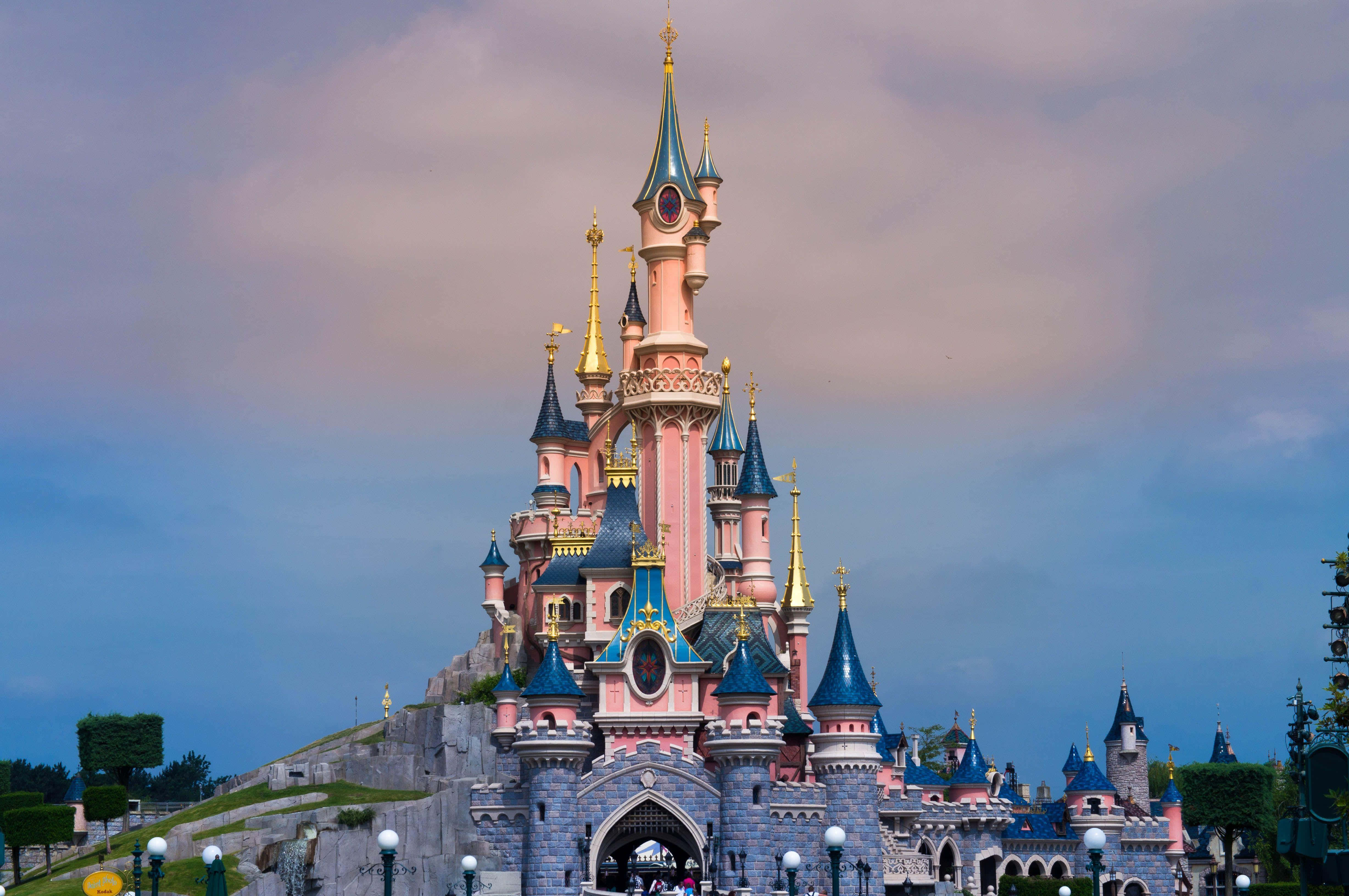 Disneyland Castle 桌布 壁紙 — 一座宏偉的粉藍色城堡，金色尖塔聳立在柔和的暮色天空中。