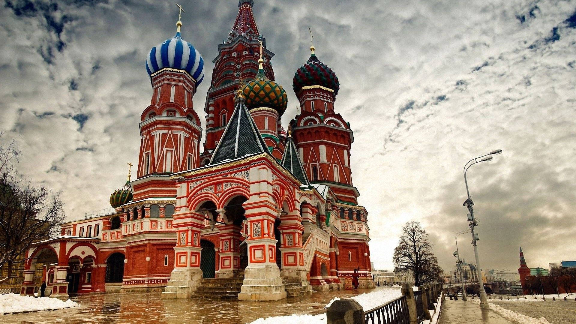 Russia 桌布 壁紙 — 一座宏偉的紅白相間大教堂，帶有色彩繽紛的洋蔥形圓頂，矗立在戲劇性的多雲天空下，地面積雪。