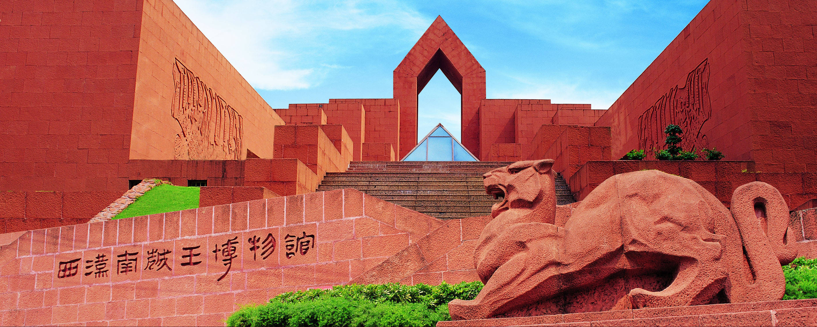 Guangzhou 桌布 壁紙 — 一座宏偉的紅磚博物館，在晴朗的藍天下，有一尊咆哮的獅子雕塑和漢字。
