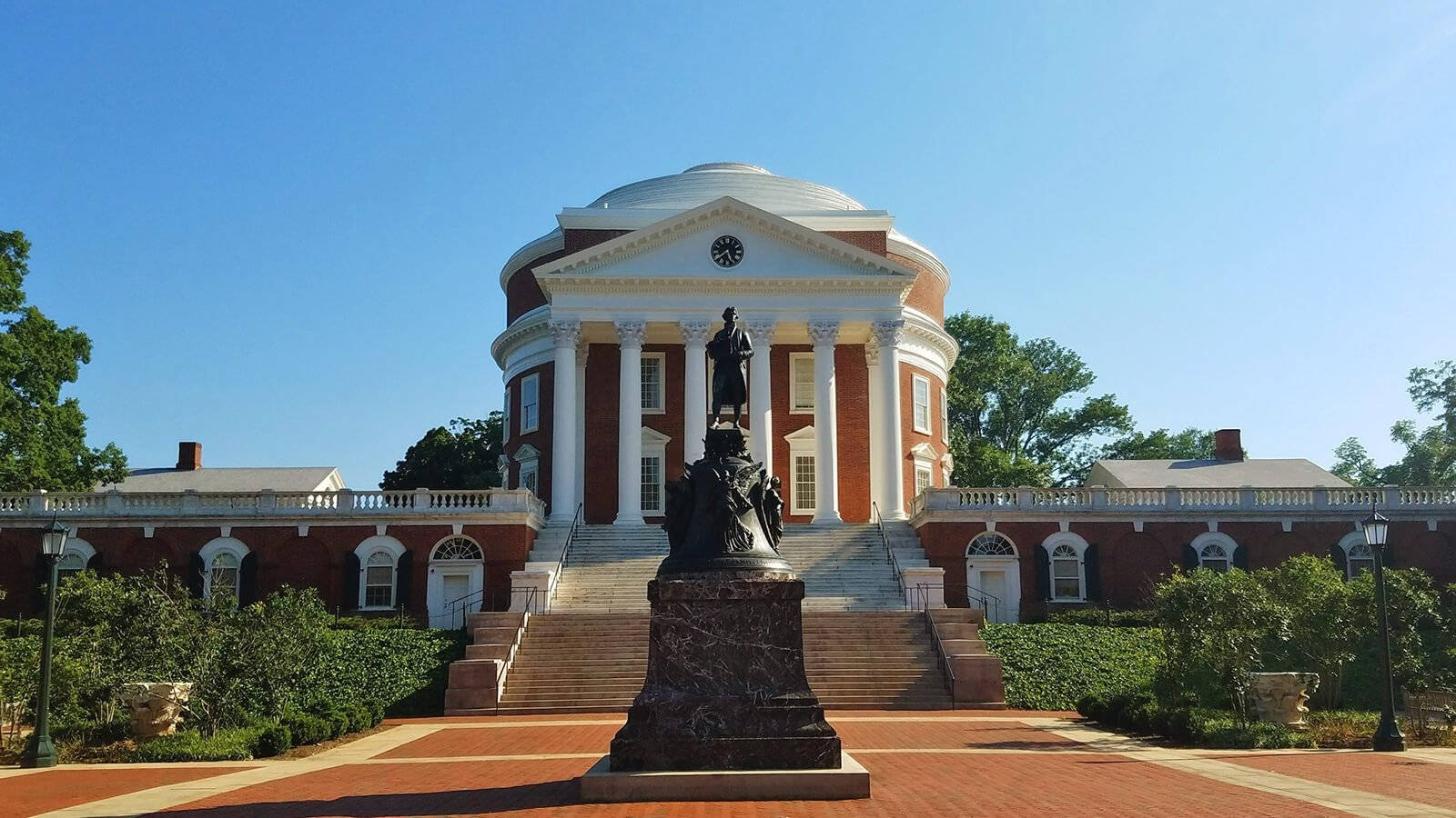 Virginia 桌布 壁紙 — 一座宏偉的紅磚圓形大廳，配有白色柱子和圓頂，矗立在清澈的藍天下，兩旁是綠樹和中央大理石基座上的雕像。