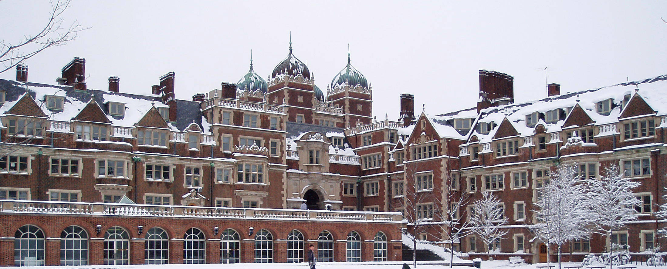 雪 桌布 壁紙 — 一座宏偉的紅磚大學建築，擁有積雪的圓頂和光禿的樹木，在陰沉的冬日天空下。