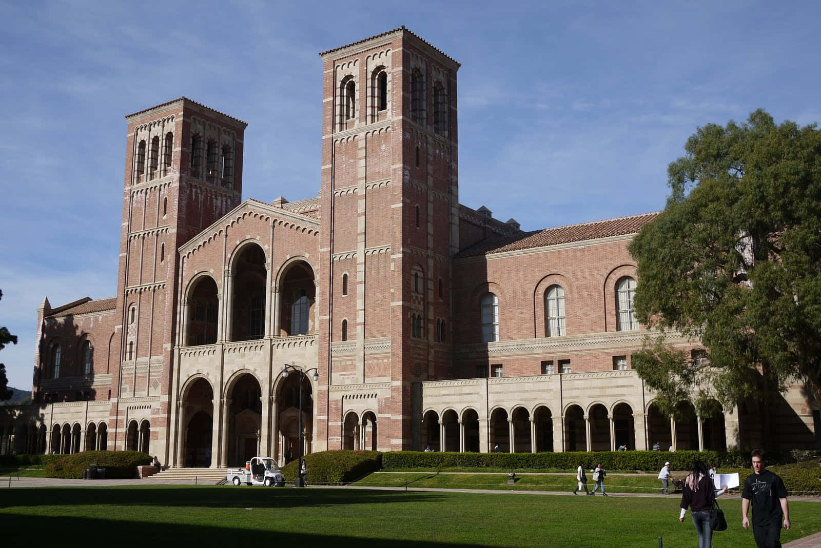 Ucla Campus 桌布 壁紙 — 一座宏偉的紅磚大學建築，擁有雙塔和拱形步道，在晴朗的藍天下。