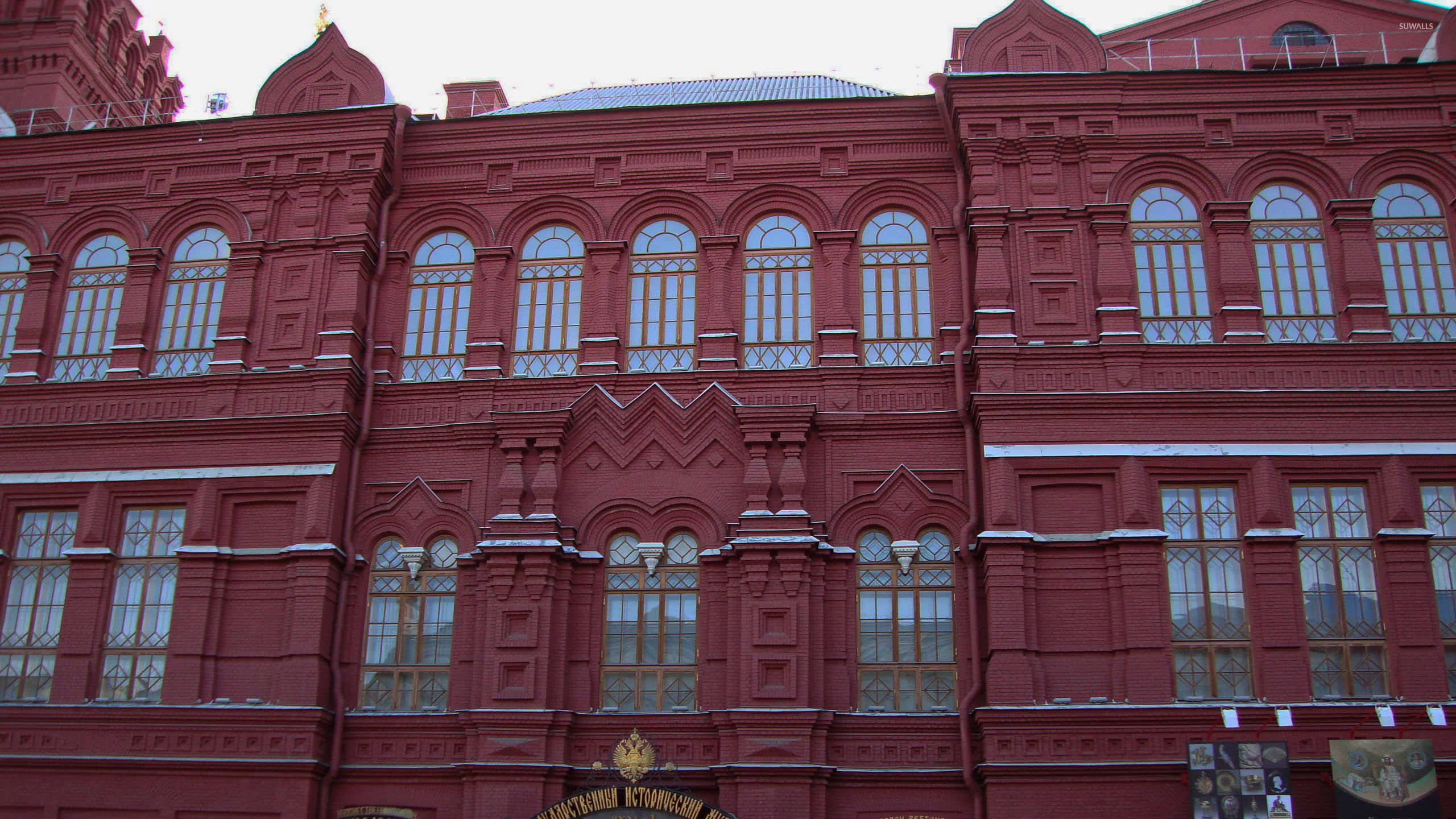 Museums 桌布 壁紙 — 一座宏偉的紅磚建築，擁有華麗的窗戶和積雪的窗台，在蒼白的冬日天空下。