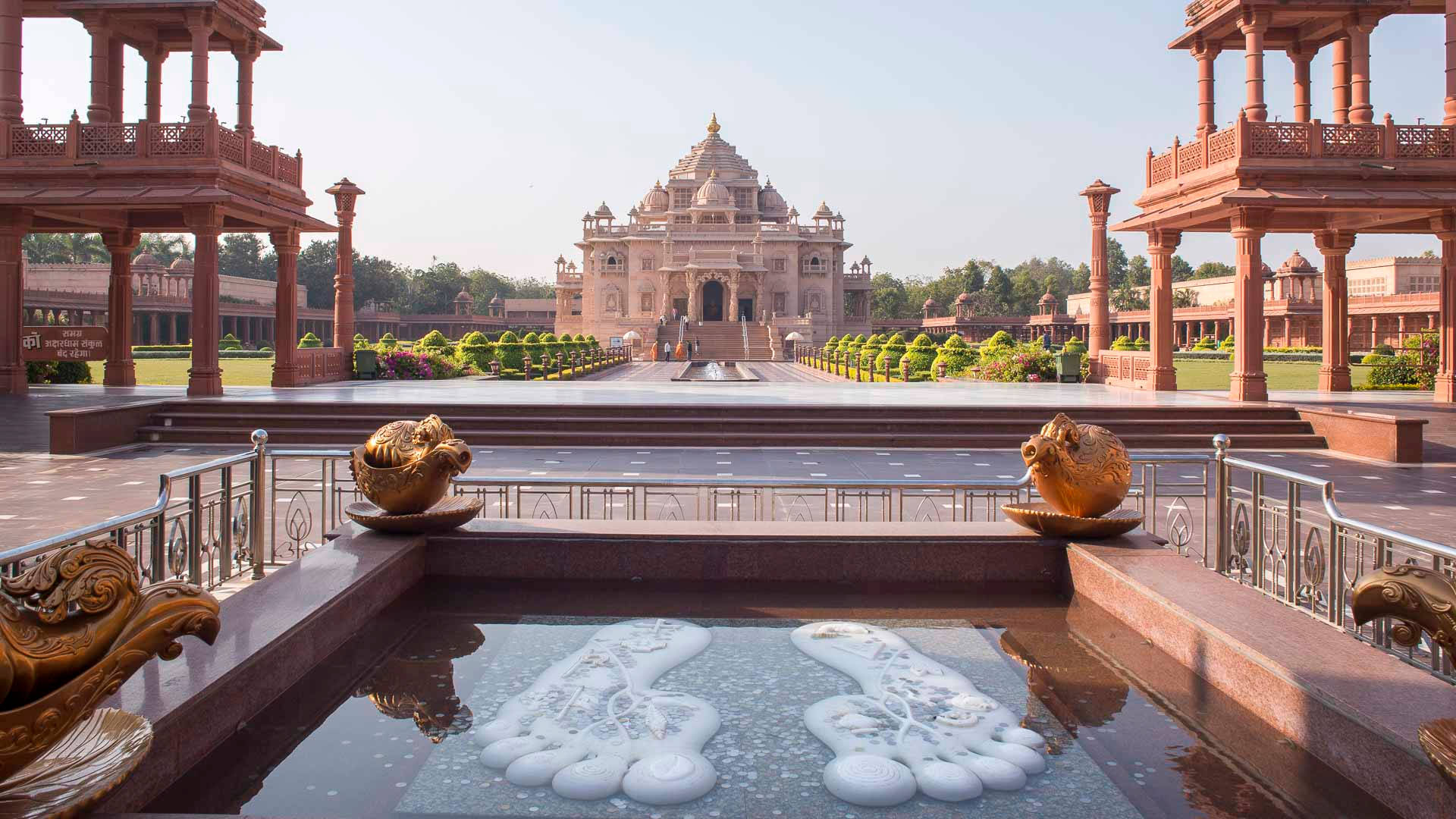 Ahmedabad 桌布 壁紙 — 一座宏偉的紅色砂岩寺廟建築群，擁有對稱的庭院和華麗的金色雕塑，兩旁襯托著一個反射水池。