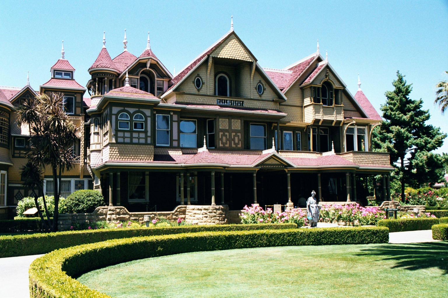 Mansion 桌布 壁紙 — 一座宏偉的維多利亞式大宅，擁有紅色瓦片屋頂和華麗的木工，矗立在修剪整齊的花園中，上方是清澈的藍天。