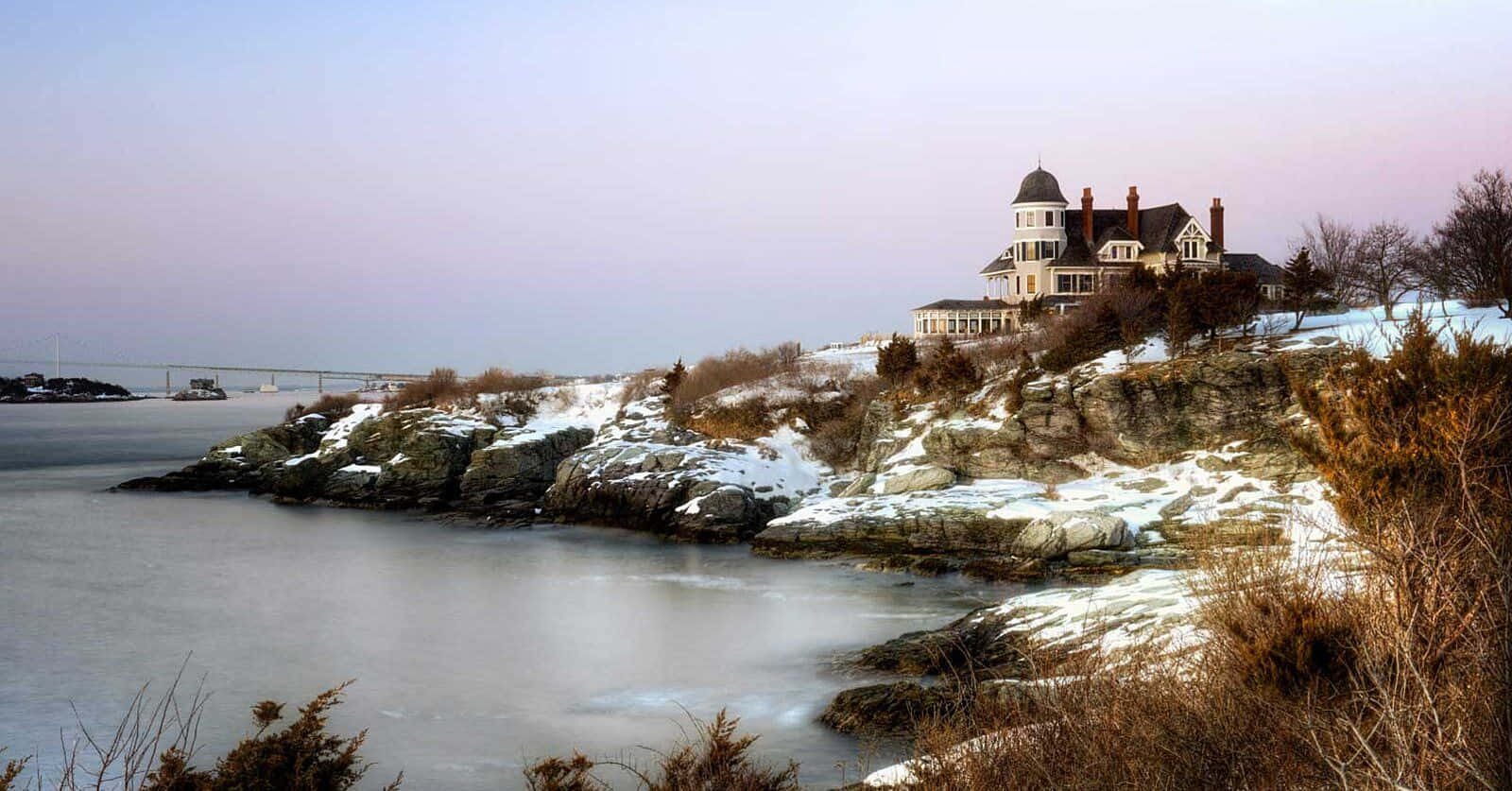 Winter Beach 桌布 壁紙 — 一座宏偉的維多利亞式房屋坐落在白雪覆蓋的懸崖上，俯瞰著黃昏時平靜的冬日大海。