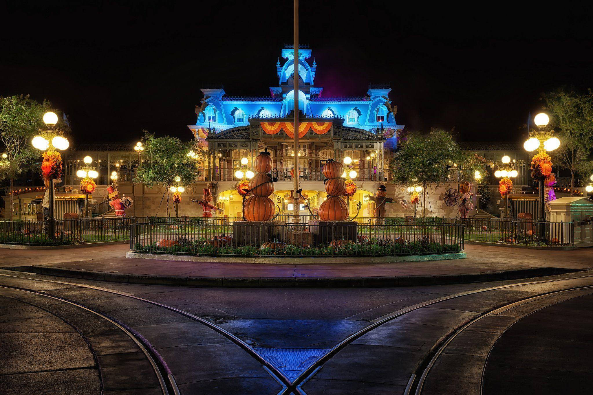 Universal Studios 桌布 壁紙 — 一座宏偉的萬聖節主題建築，夜晚以藍色和橙色燈光點亮，前景有南瓜裝飾和電車軌道。