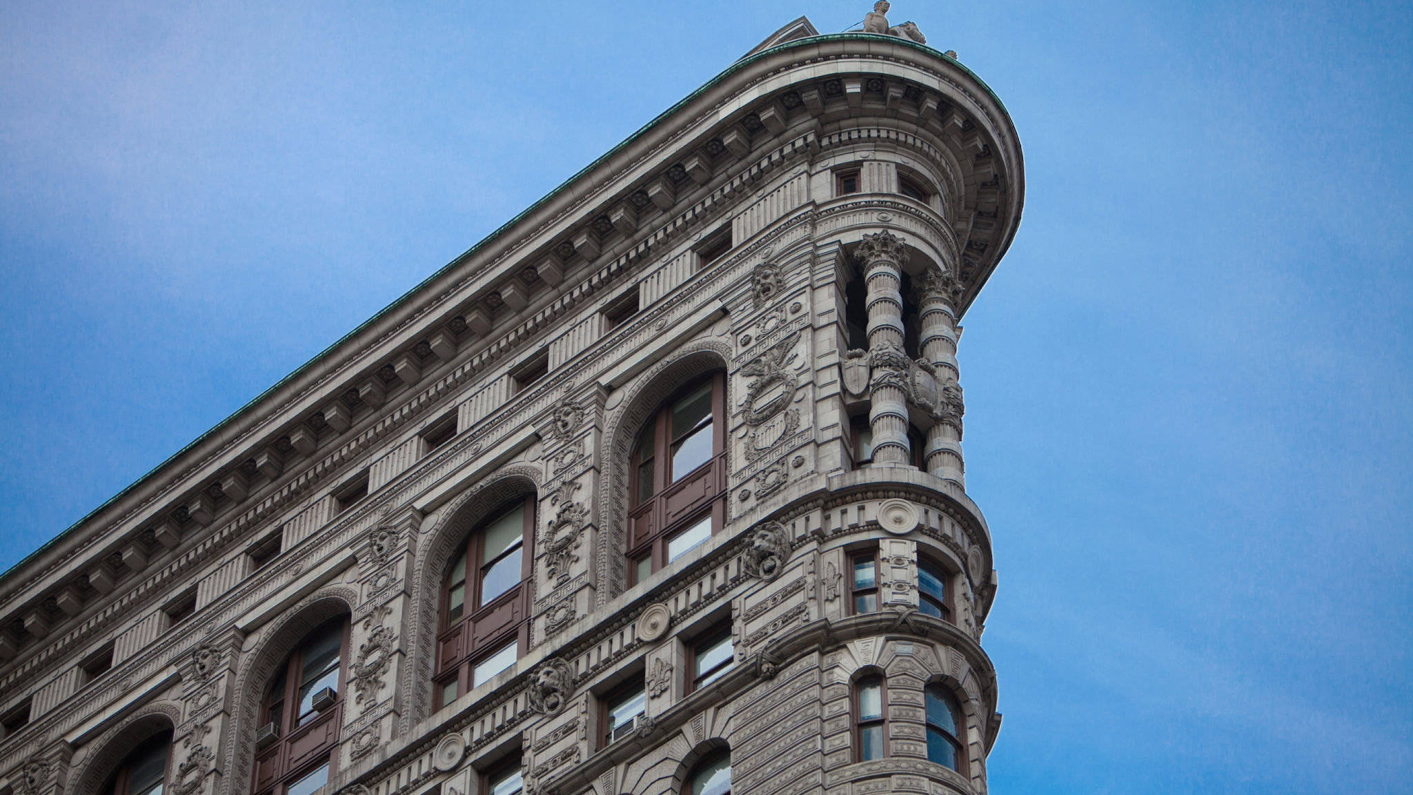 Flatiron Building 桌布 壁紙 — 一座宏偉的裝飾性石造建築，帶有拱形窗戶和精緻雕刻，在清澈的藍天下聳立。