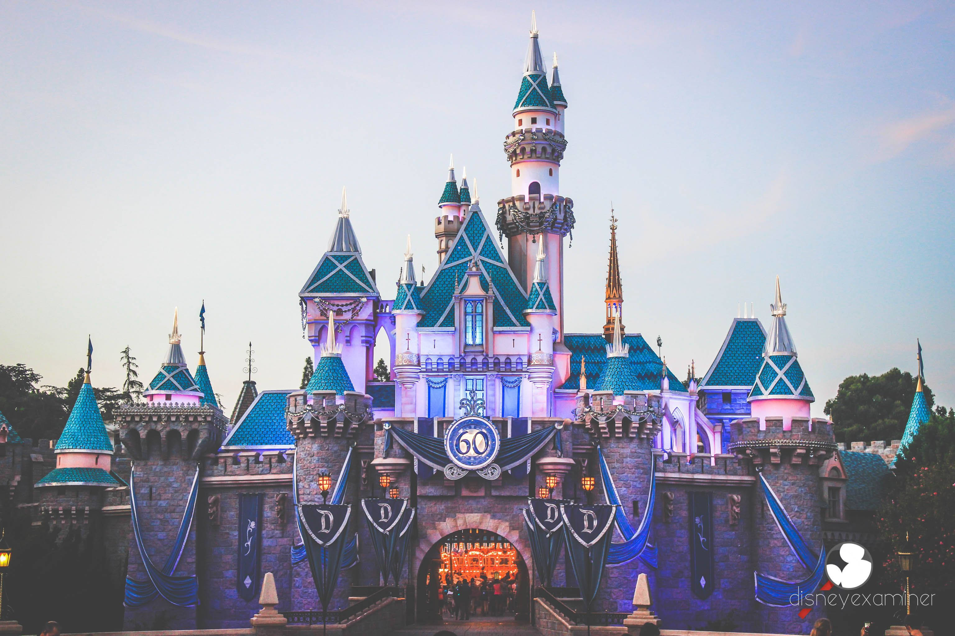 Disney Castle 桌布 壁紙 — 一座宏偉的迪士尼城堡，在柔和的暮色天空下，被紫色和藍色燈光照亮。