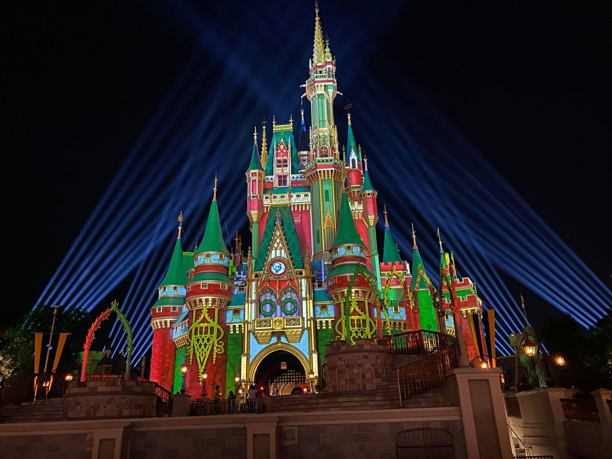 Disney Castle 桌布 壁紙 — 一座宏偉的迪士尼城堡，在漆黑的夜空下被鮮豔的燈光和戲劇性的藍色聚光燈照亮。