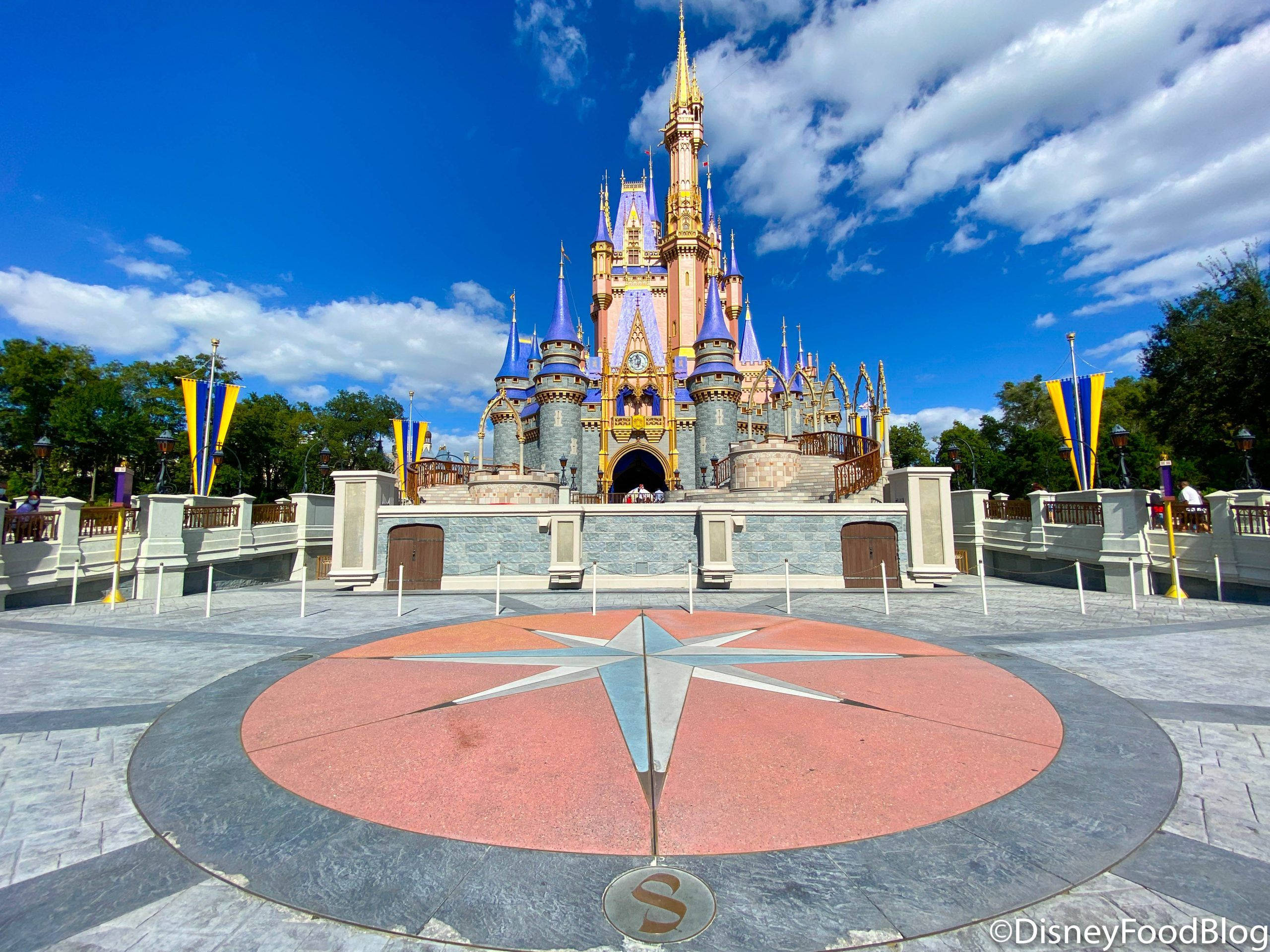 Walt Disney World 桌布 壁紙 — 一座宏偉的迪士尼城堡，擁有藍色尖頂和金色點綴，矗立在晴朗的藍天下，白雲朵朵。