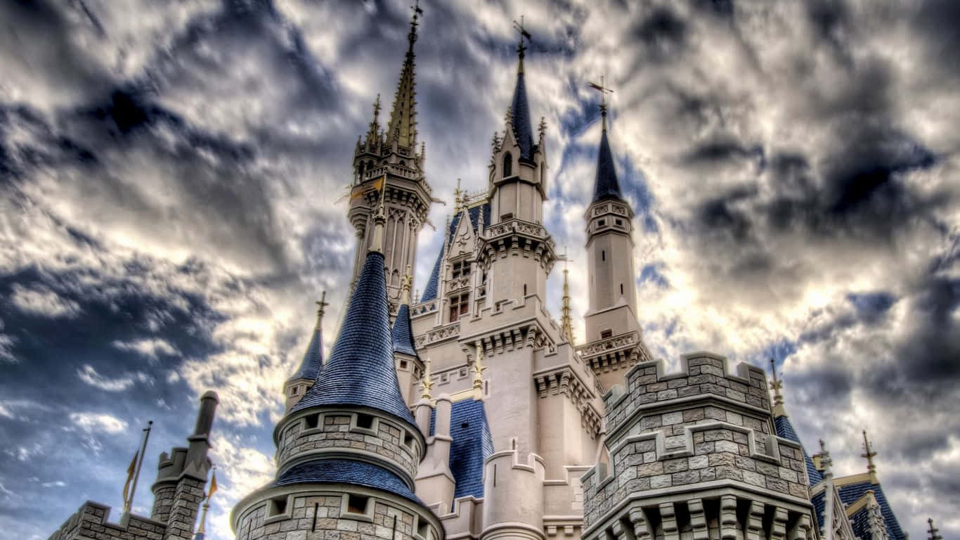 Cinderella Castle 桌布 壁紙 — 一座宏偉的迪士尼城堡，擁有藍色尖頂和石塔，聳立在戲劇性的多雲天空下。