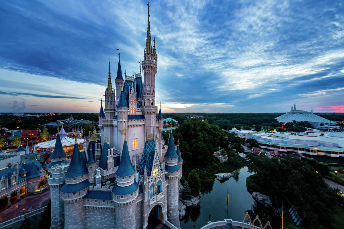 Disneyworld 桌布 壁紙 — 一座宏偉的迪士尼城堡，窗戶閃閃發光，聳立在帶有粉紅色和藍色雲彩的暮色天空中。