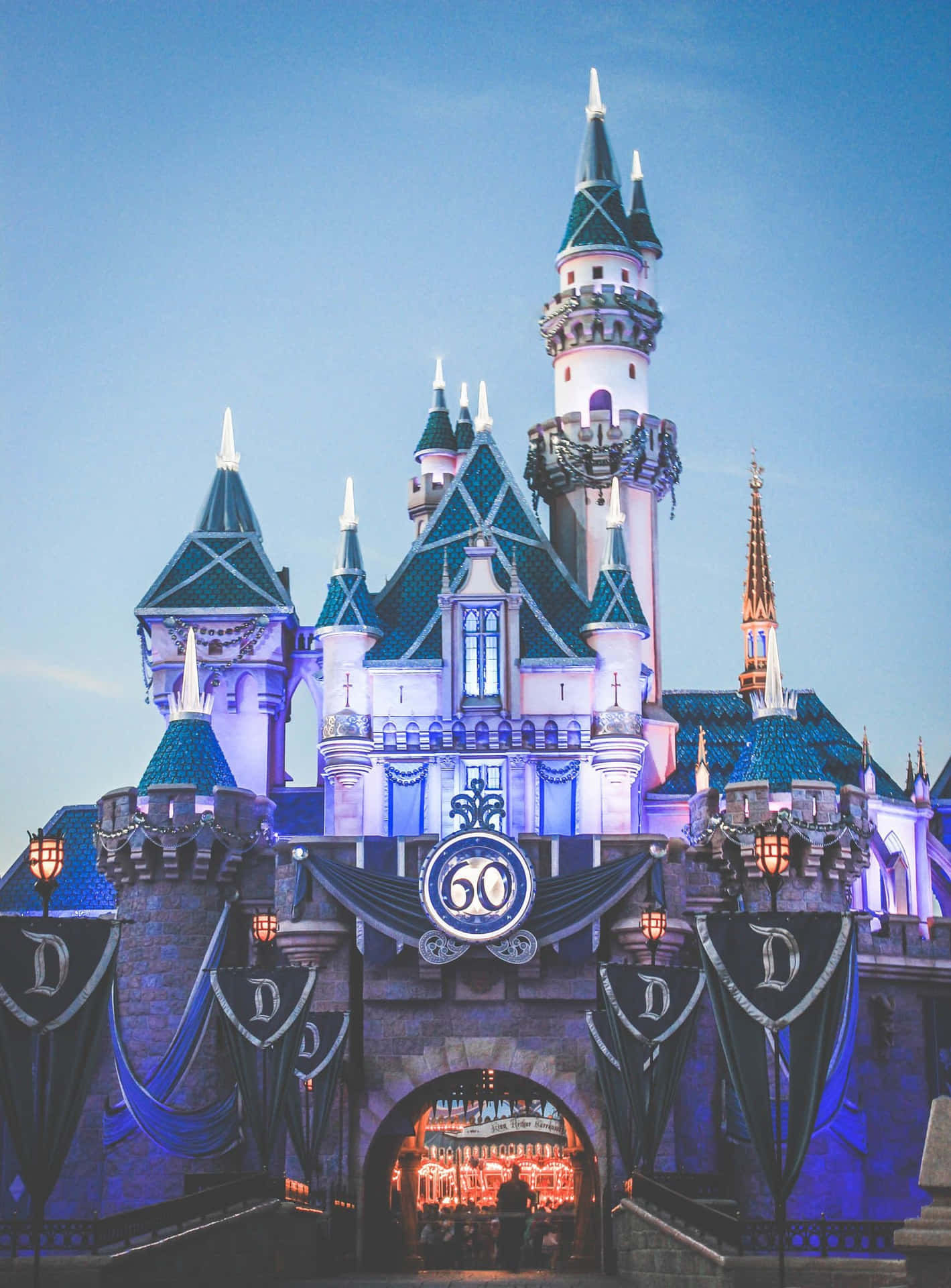 Disney Castle 桌布 壁紙 — 一座宏偉的迪士尼城堡在暮色天空下以紫色和藍色燈光點亮，並帶有「60」週年紀念標誌。