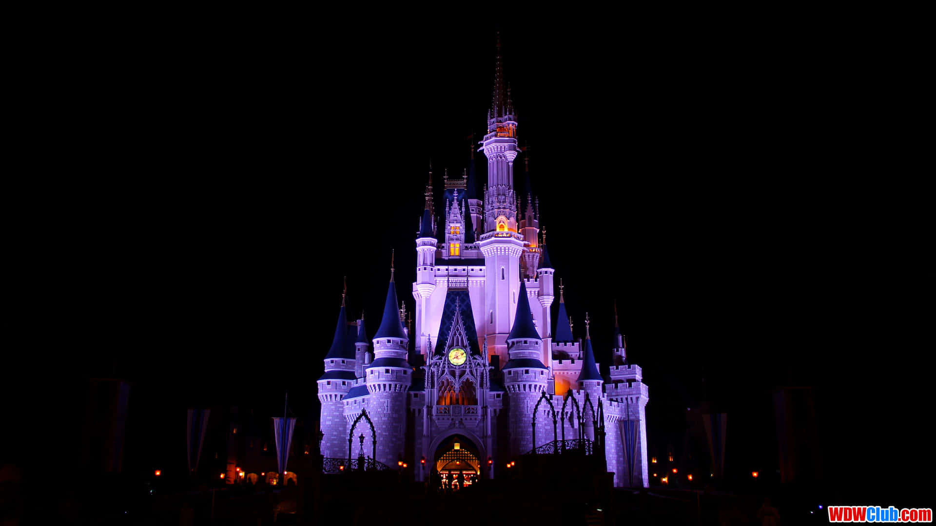 Disney World Desktop 桌布 壁紙 — 一座宏偉的迪士尼城堡在漆黑的夜空中被紫色和金色的燈光照亮。