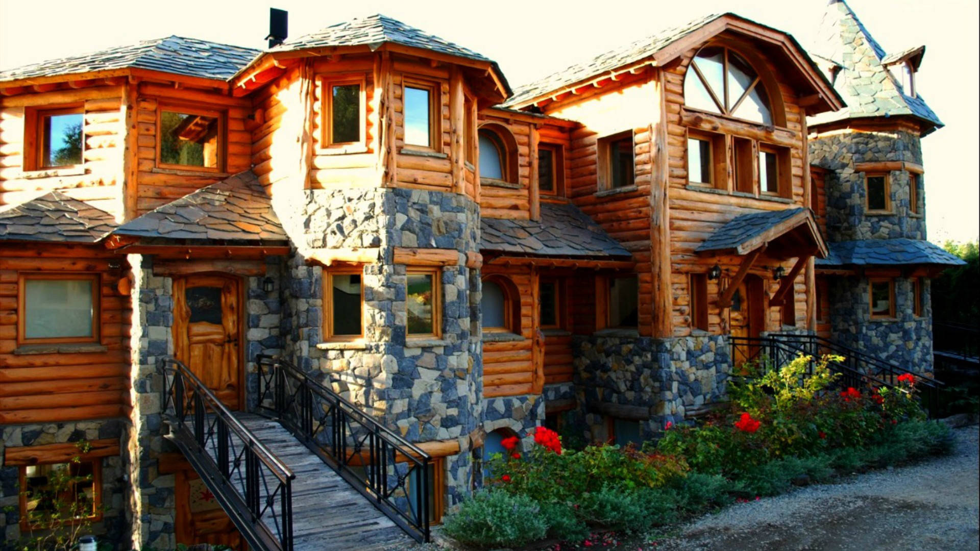 Wood House 桌布 壁紙 — 一座宏偉的鄉村木屋，帶有石頭裝飾和木製陽台，沐浴在溫暖的金色陽光下。